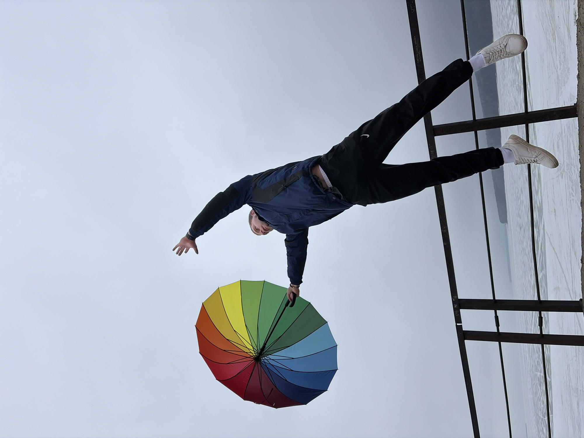 Person balances on moss-covered pipes with rainbow umbrella in Chaikovsky