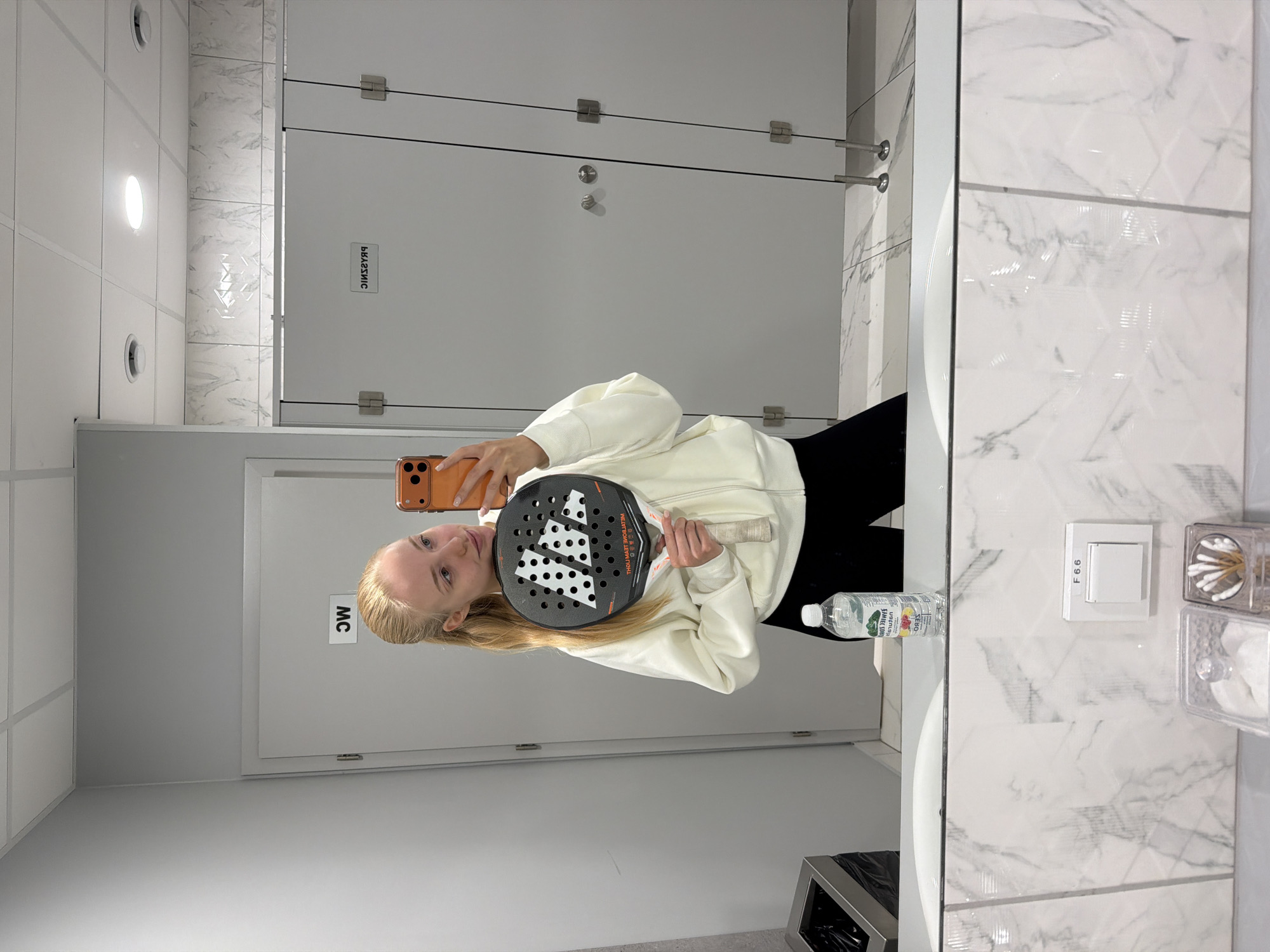 Woman takes restroom selfies with padel racket after court session