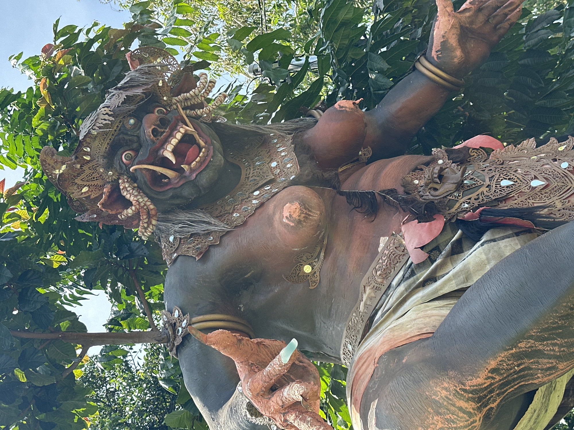Tourist documents Balinese waterfall site with demon statues, bottle art