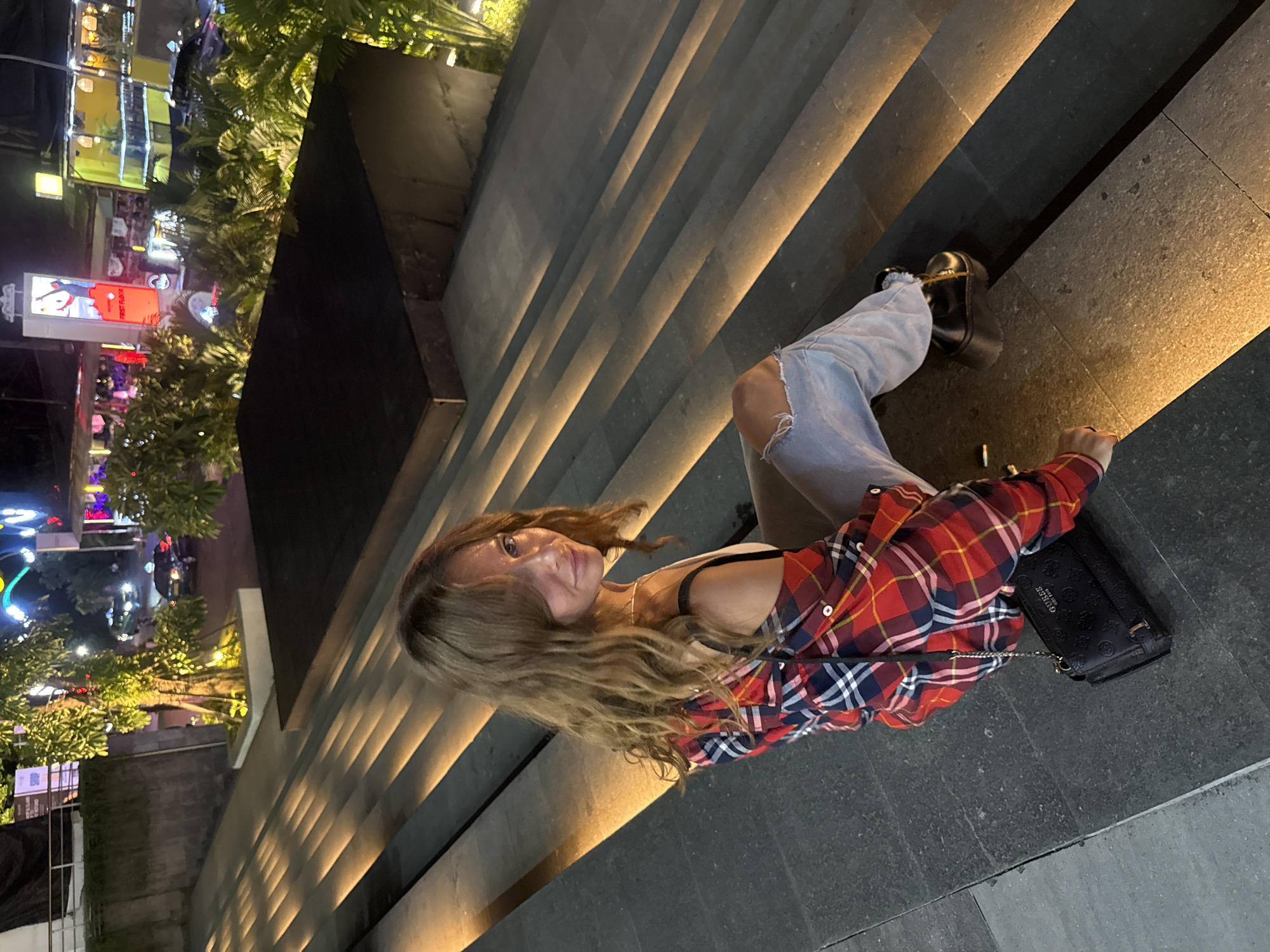 Woman in plaid shirt sits on lit stone steps in Kuta