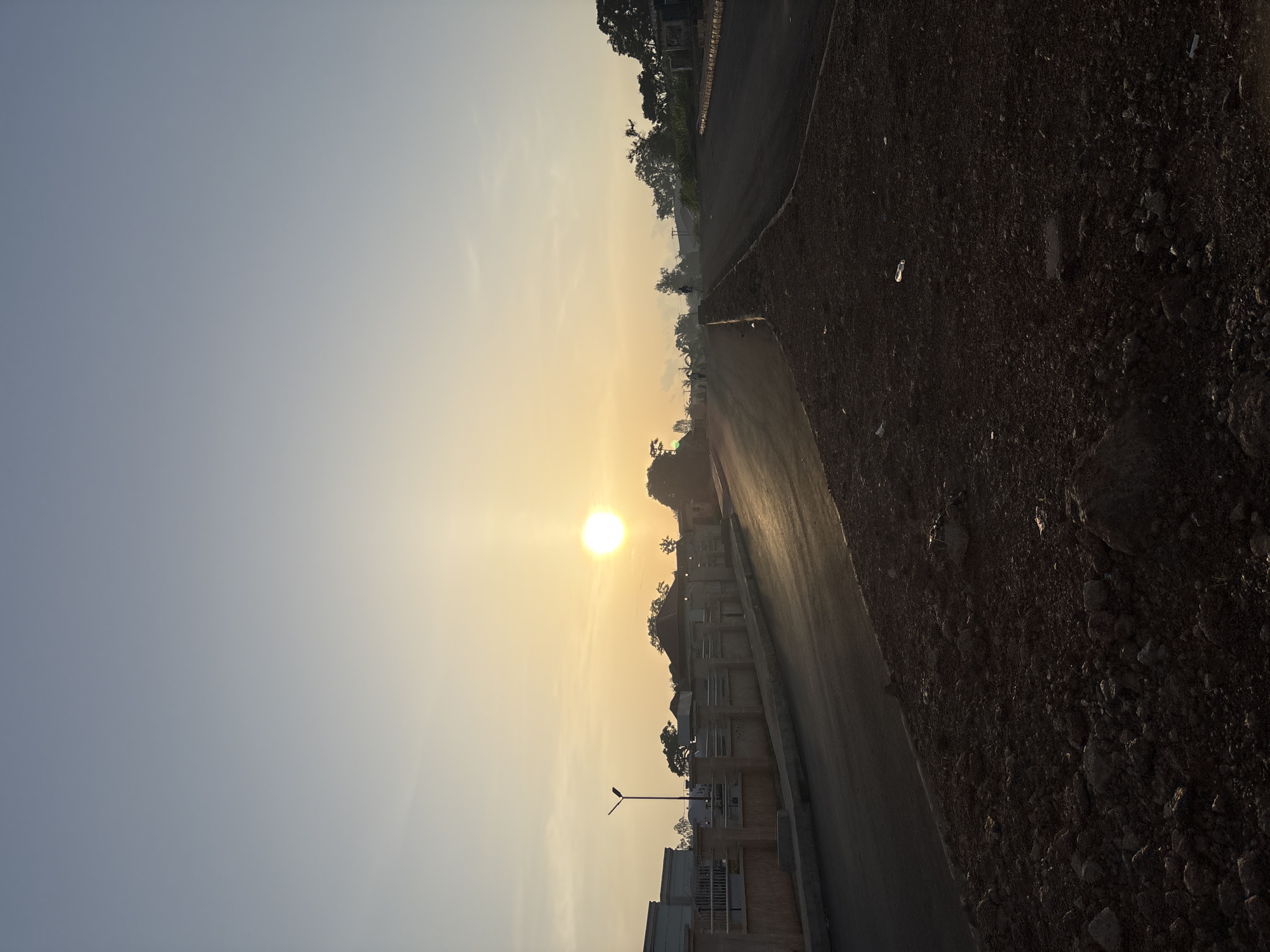 Bukuru road at sunrise, streetlights, vehicles, and low golden light