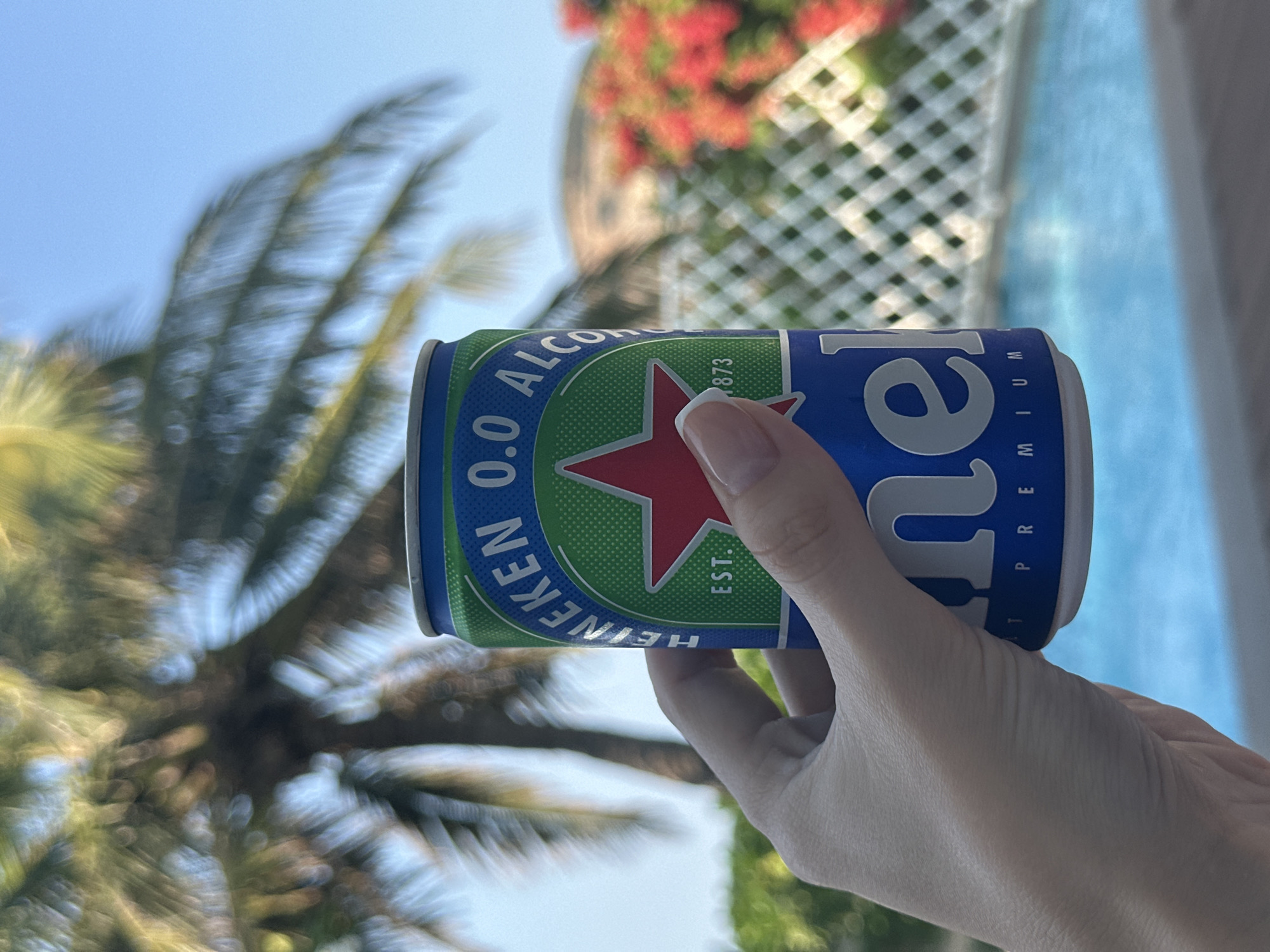 Non-alcoholic beer held at poolside location with tropical scenery