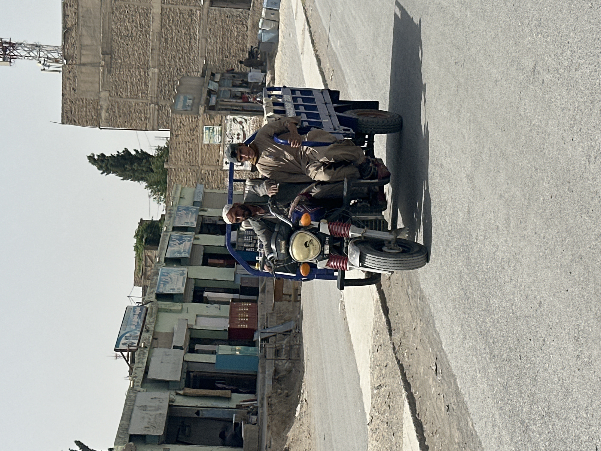 Two men ride motorcycle with trailer through Quetta streets