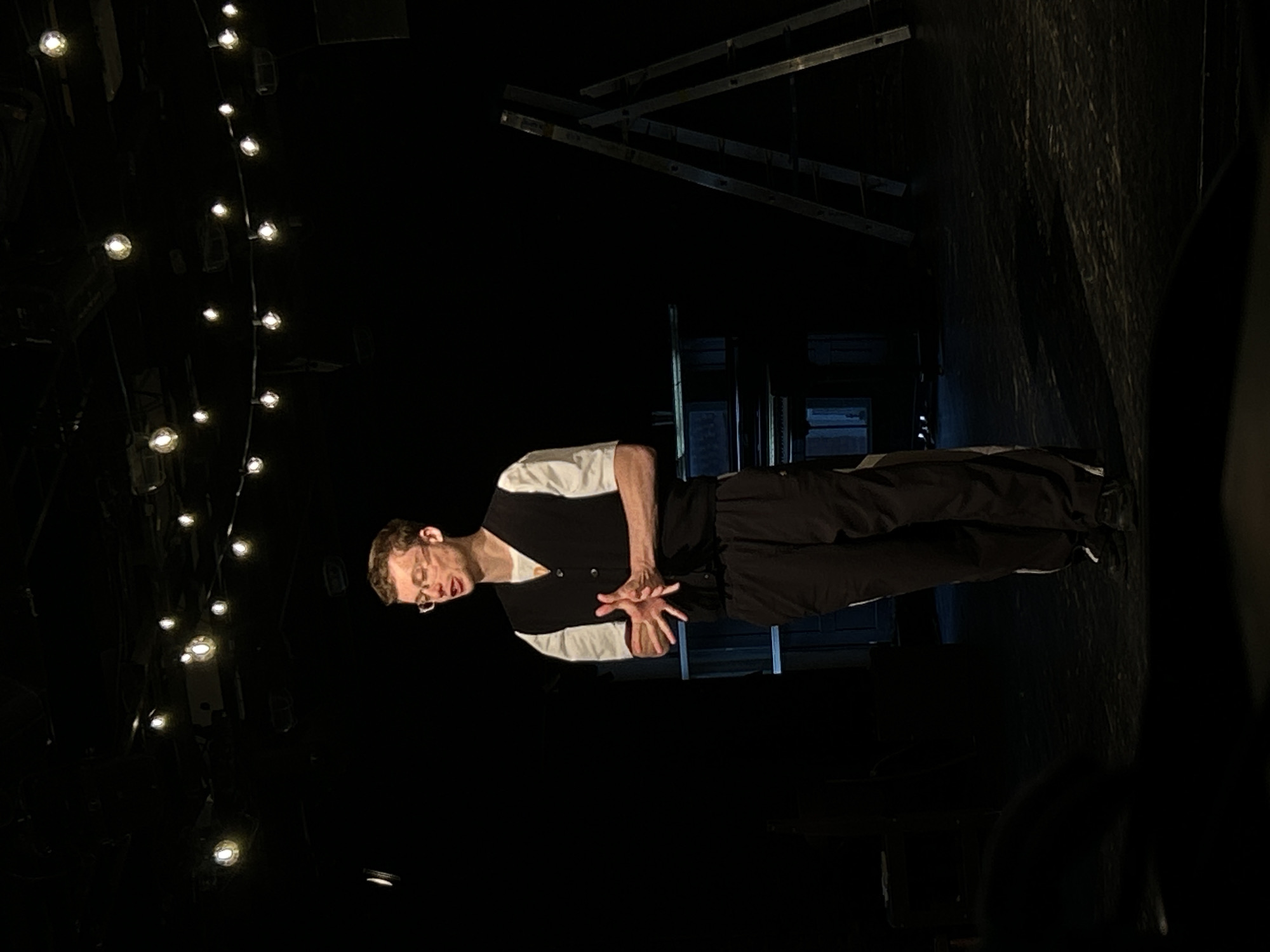 Young actor in orange sweater performs on dimly lit stage