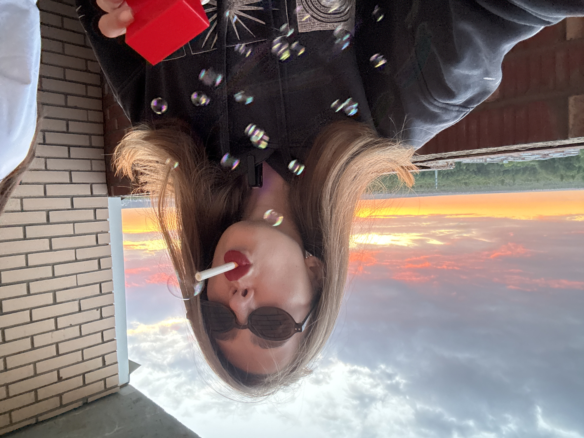 Woman takes sunset selfies, smokes and blows bubbles on rooftop