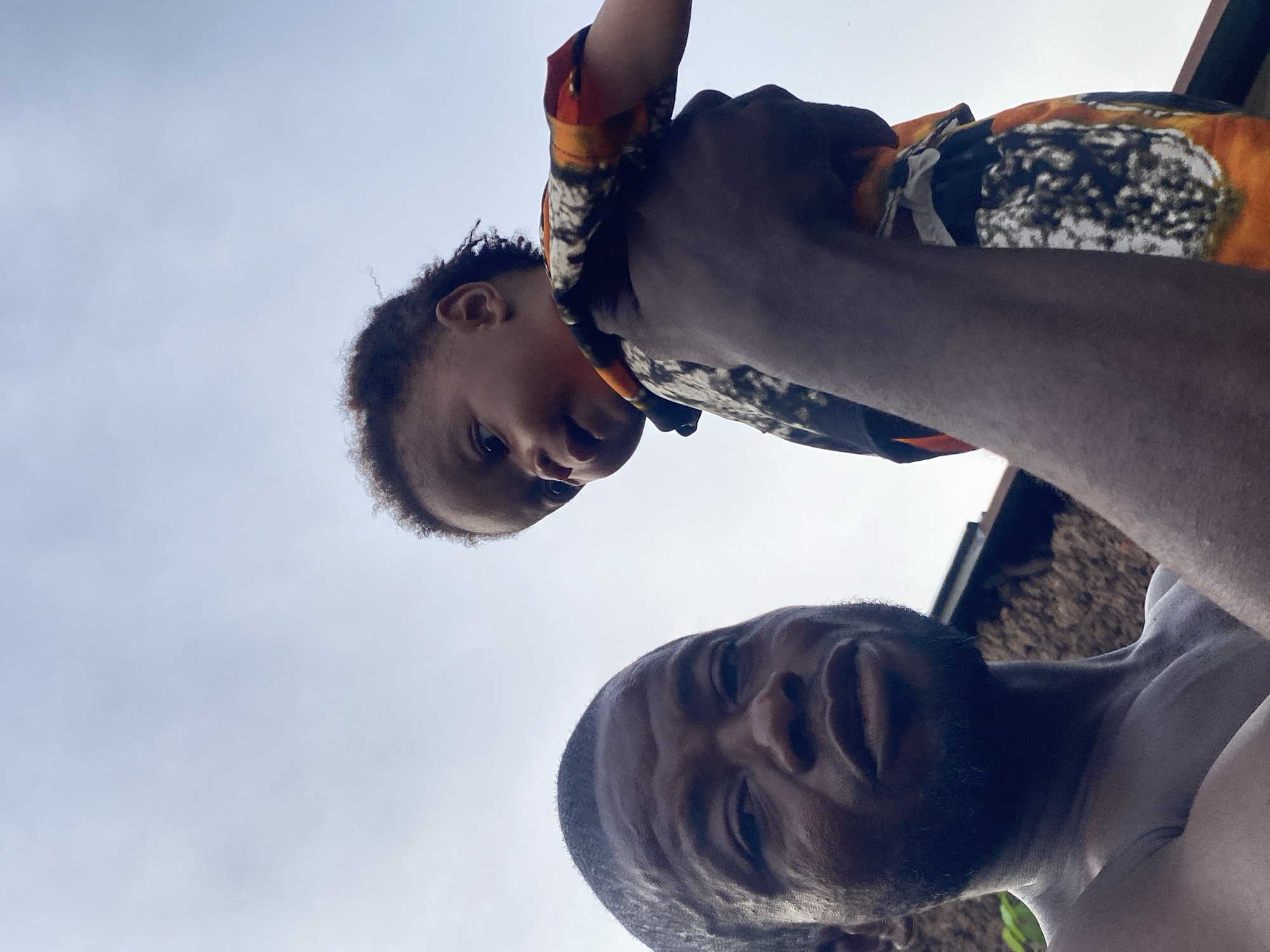 Adult and toddler photographed outdoors against open sky, Unwana