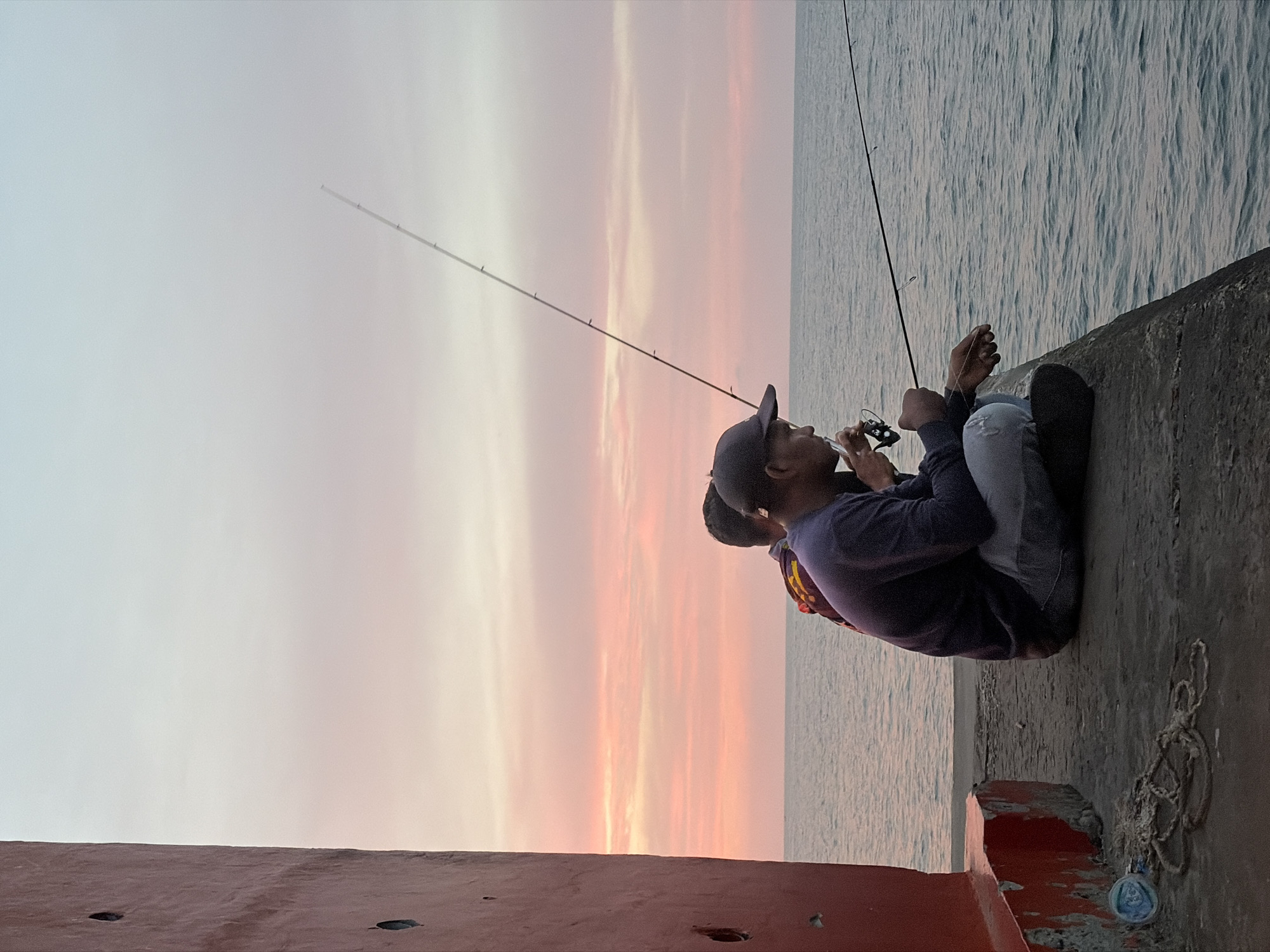 Fishing from a concrete pier at dusk in Lhokseumawe