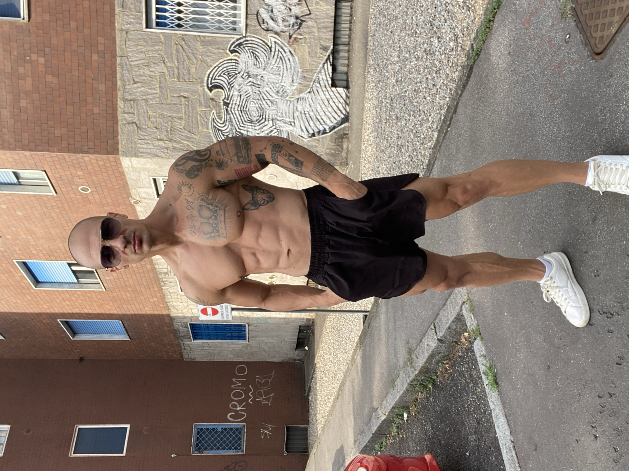Tattooed figure poses outside brick apartment building in Corsico
