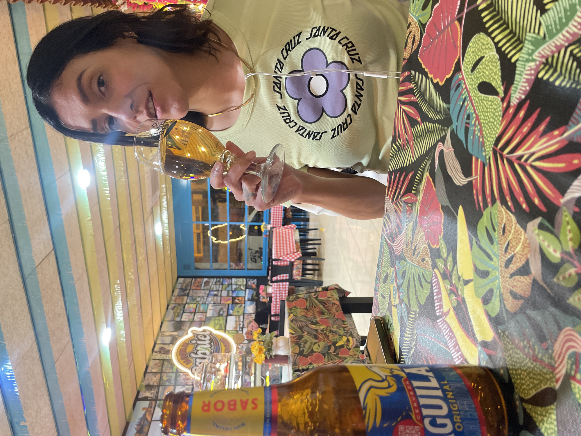 Woman enjoys Aguila beer at tropical-themed table in L'Hospitalet
