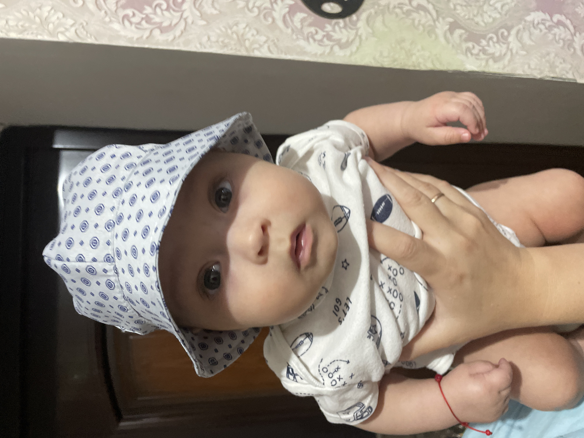Surprised baby in bucket hat held up at home in Moldova