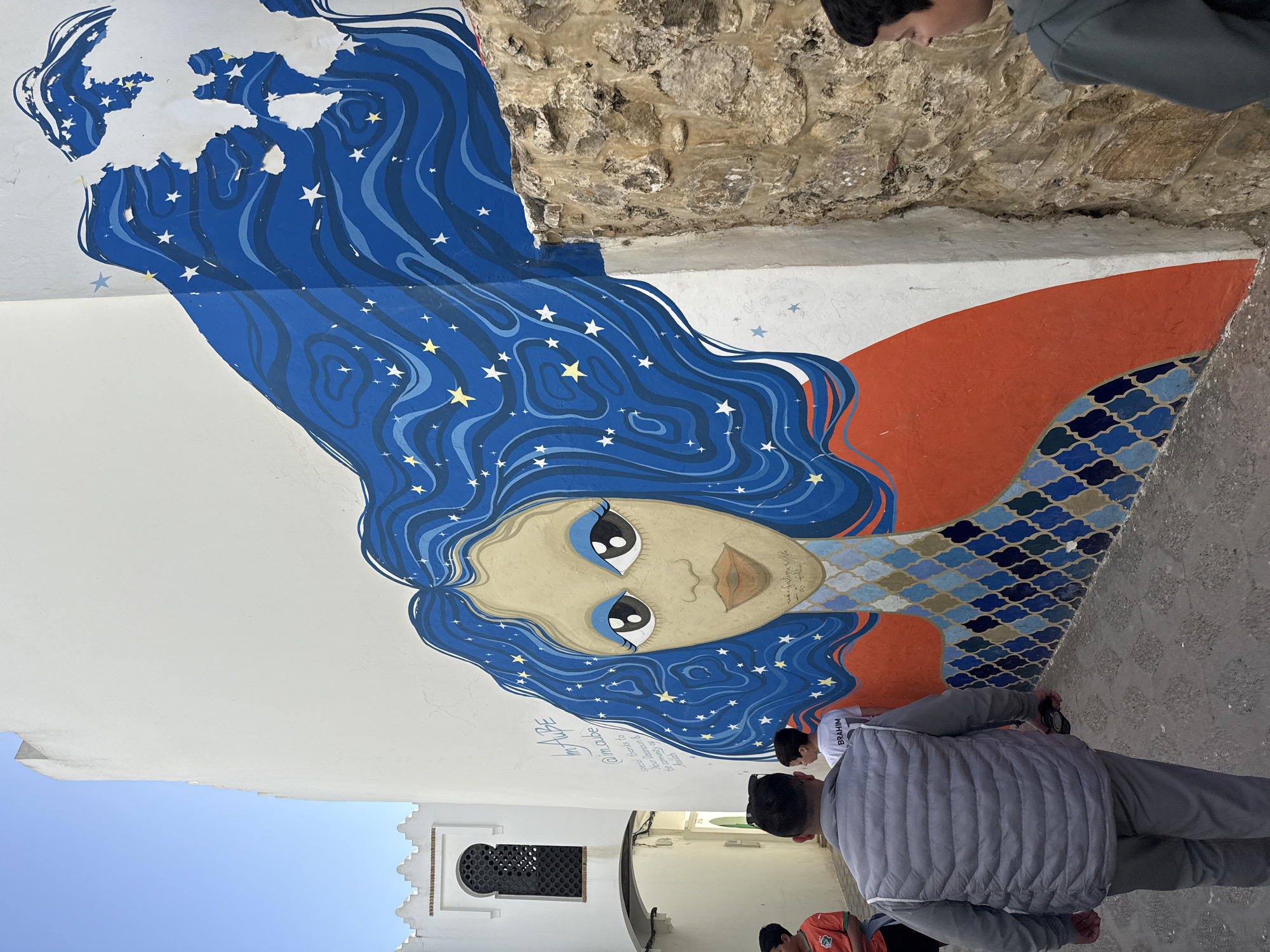 Pedestrians walk narrow streets amid murals in Asilah, Morocco