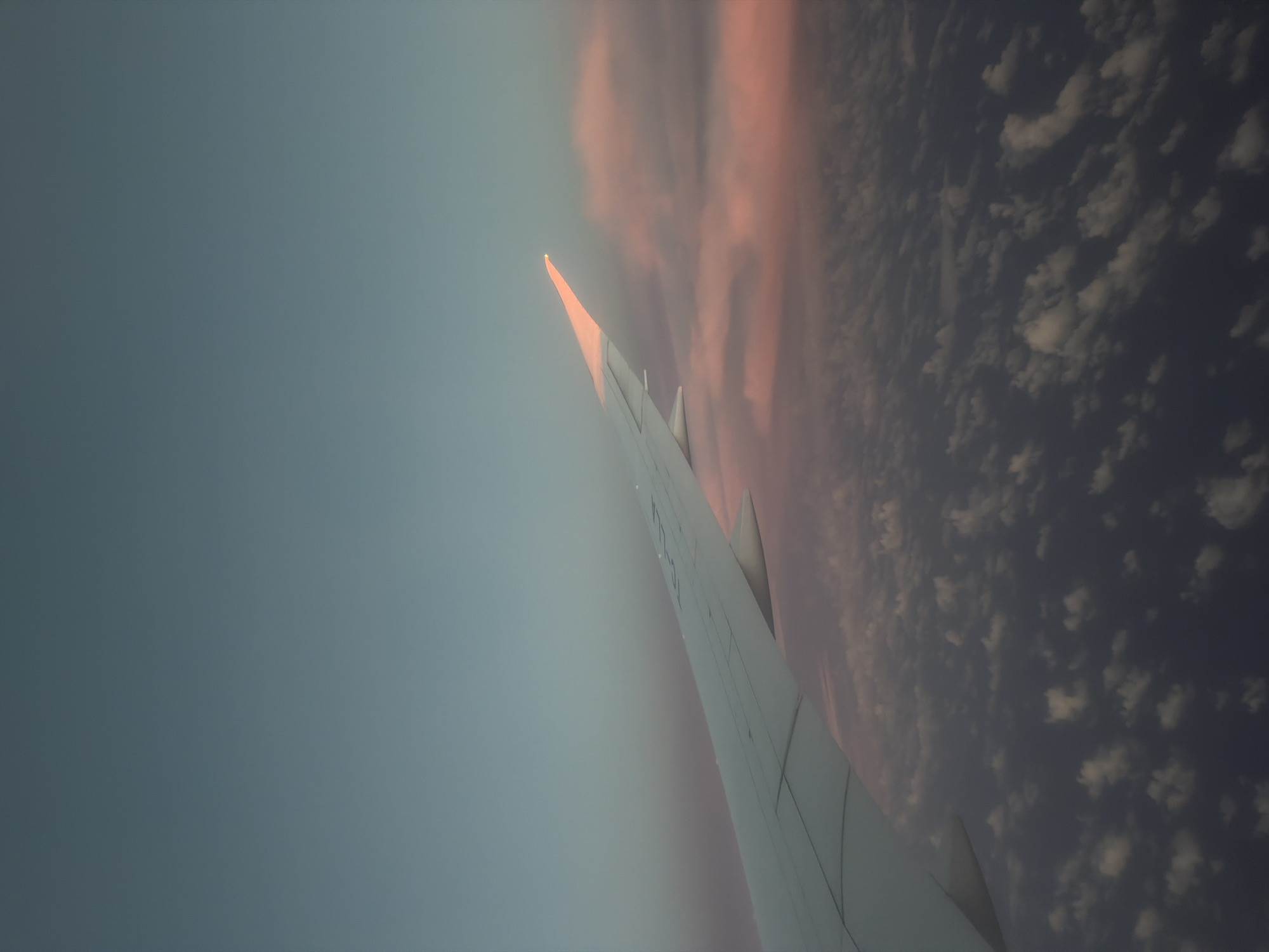 Passenger photographs airplane wing against pink-tinged clouds over Turkey