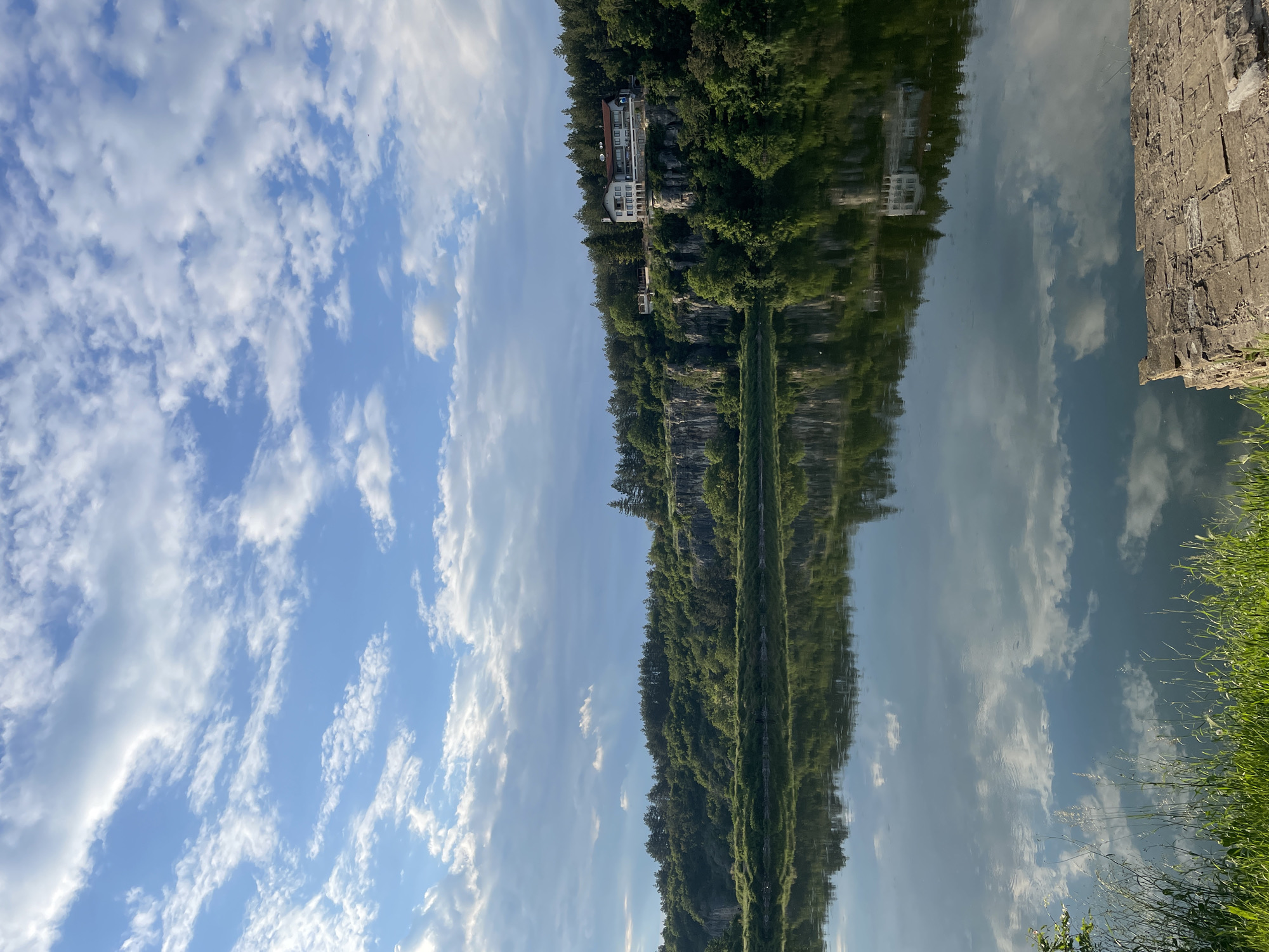 Unidentified waterfront scene with reflective water and rocky cliff documented