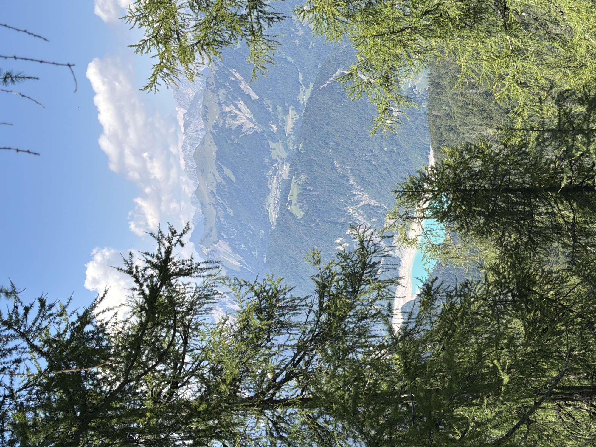 Turquoise lake and mountain peaks framed through Carnic Alps forest