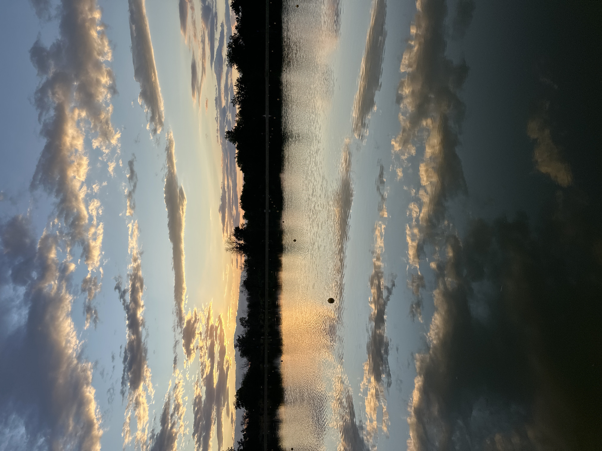 Calm lake mirrors a soft, cloudy sunset.