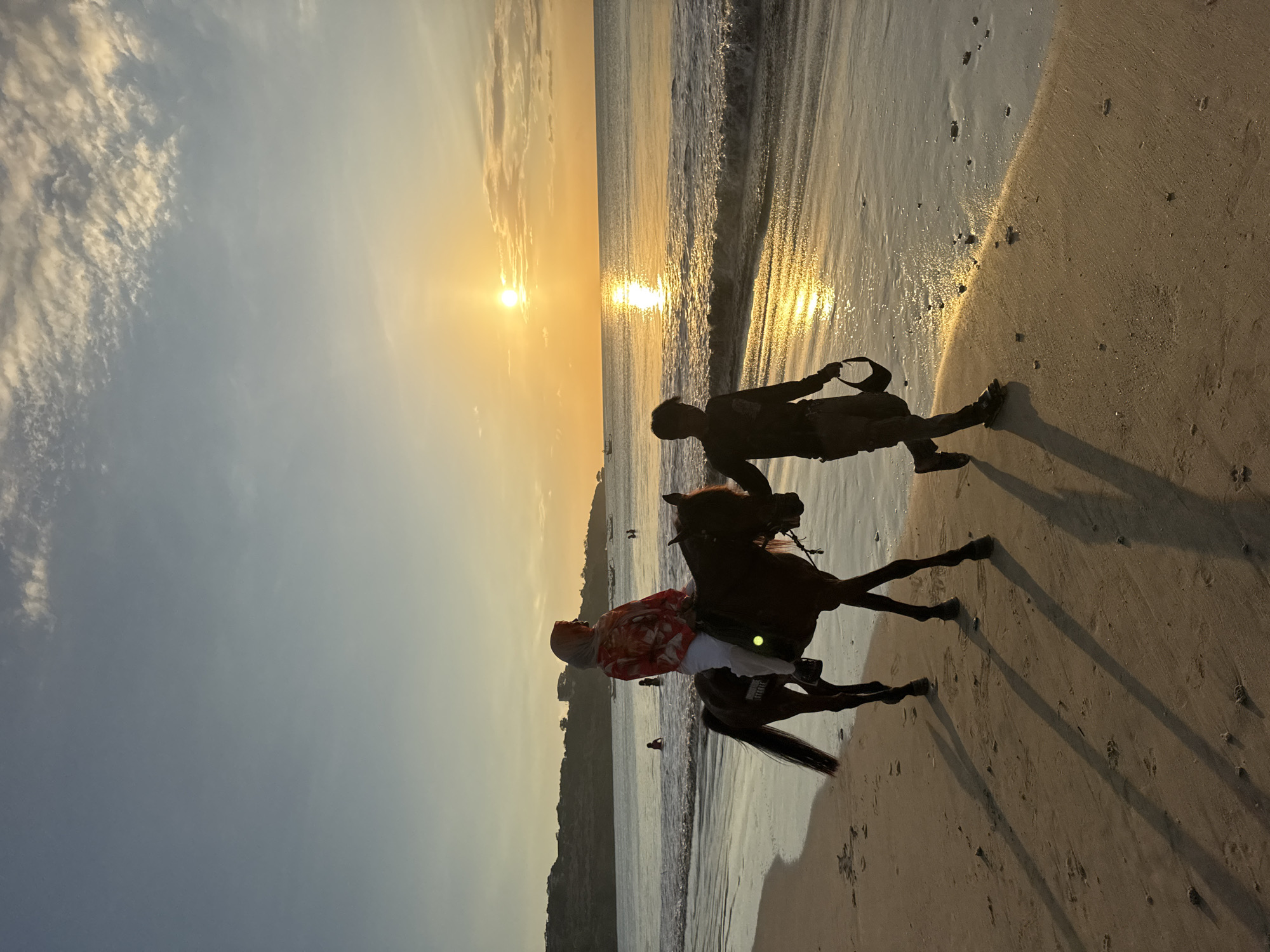 Beach sunset scene captures walker and horseback rider in Kuta