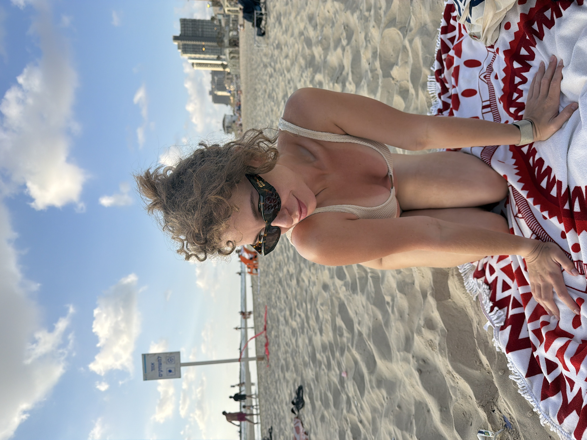 Kneeling pose on a Tel Aviv beach, city skyline behind