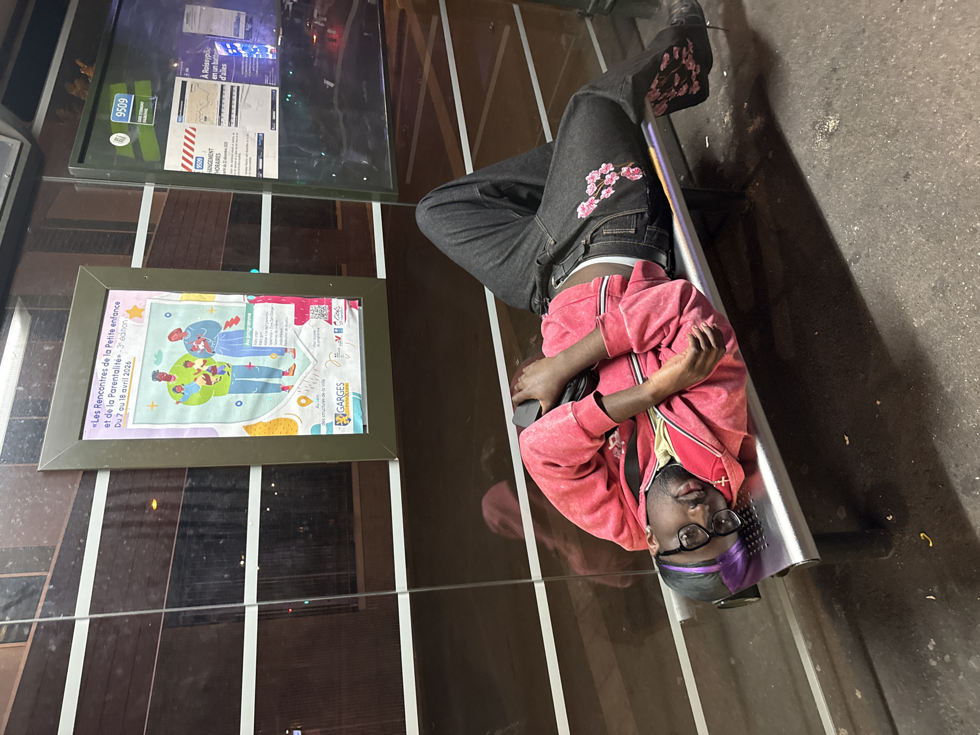 Person rests on bus stop bench in Garges-lès-Gonesse