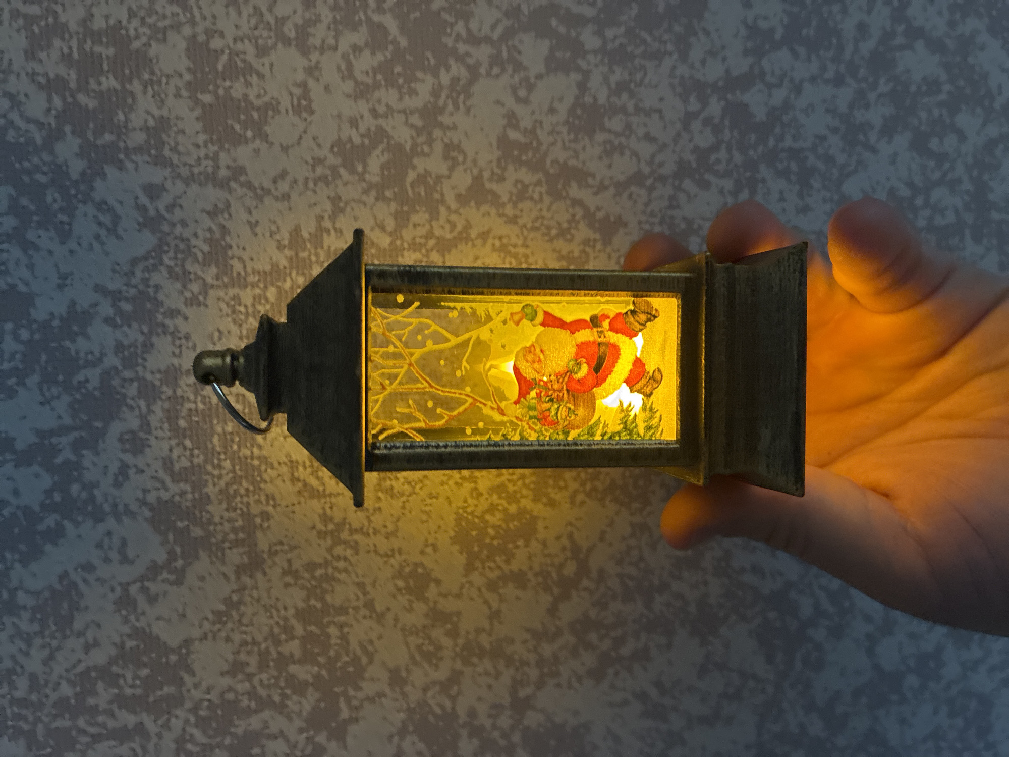 Person holds illuminated decorative lantern against textured wall