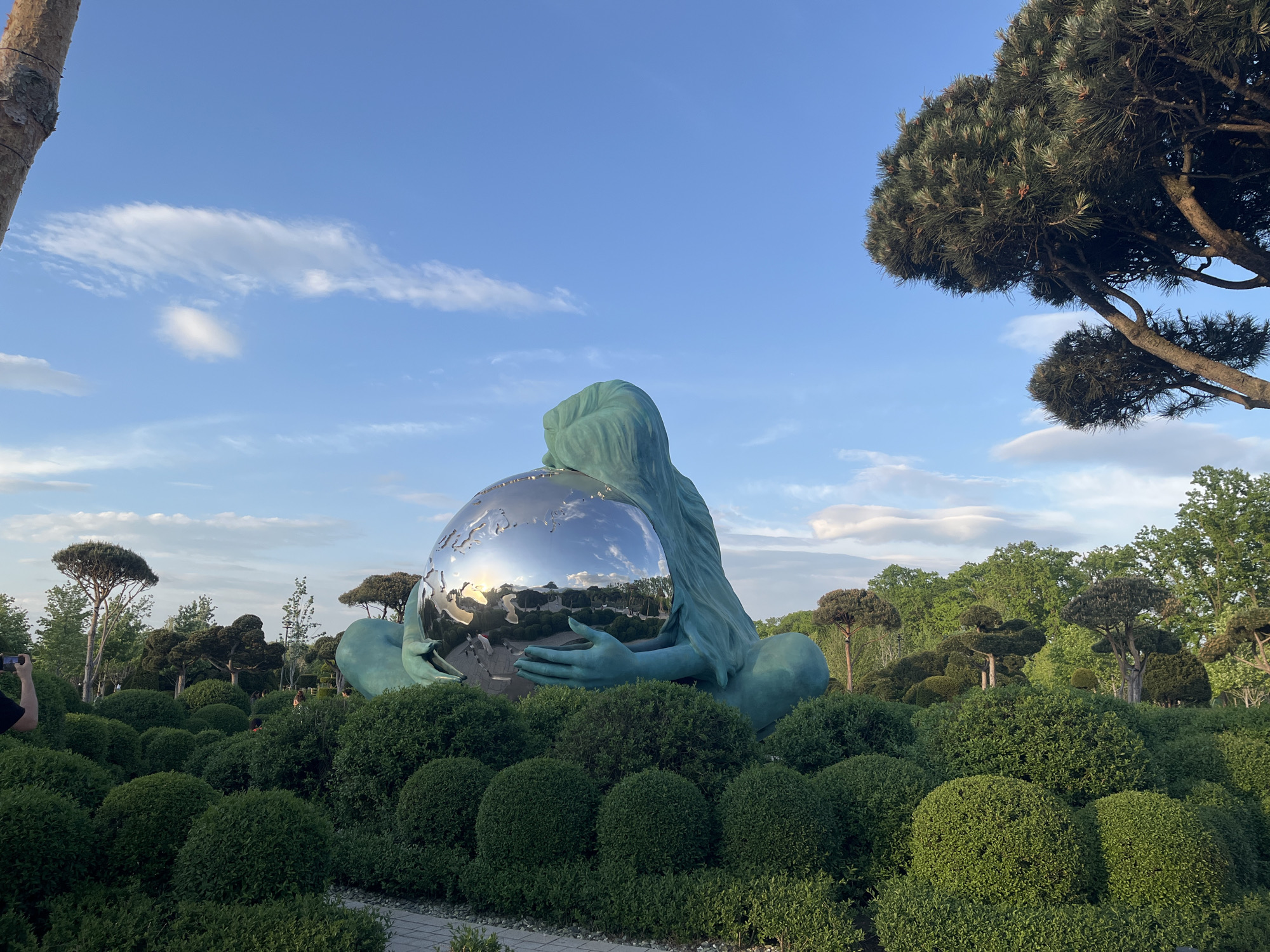 Park visitors document globe-embracing statue amid manicured gardens in Krasnodar