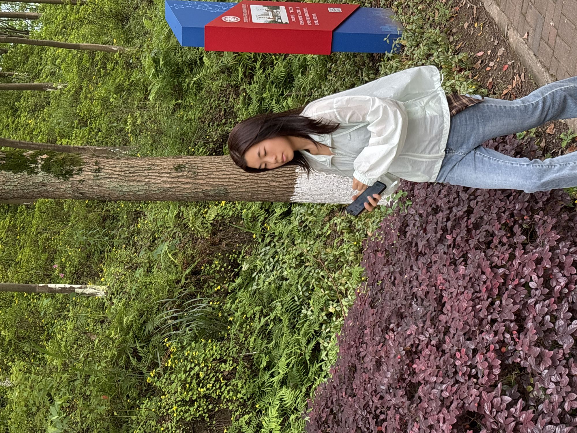 Woman rests against tree while using phone in Jiangjin