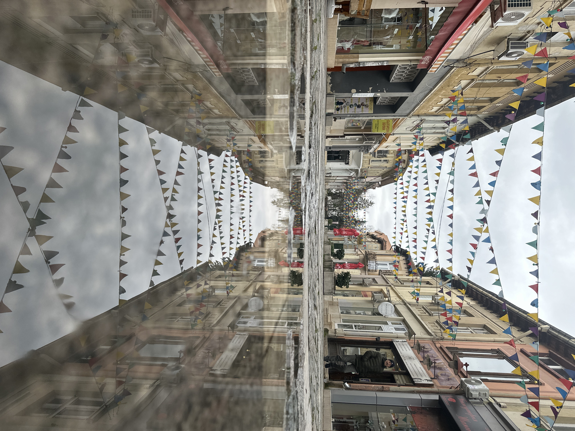 Street scene with decorative flags reflected in puddle in Vratsa