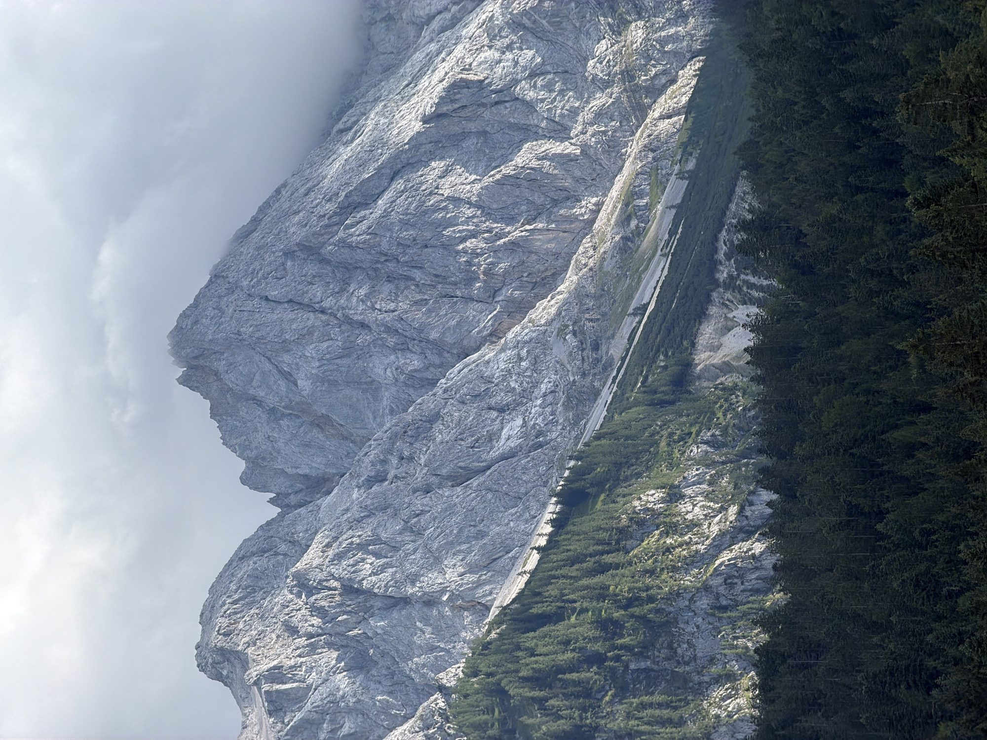 Zugspitze rises above pine forest and cloud from Grainau