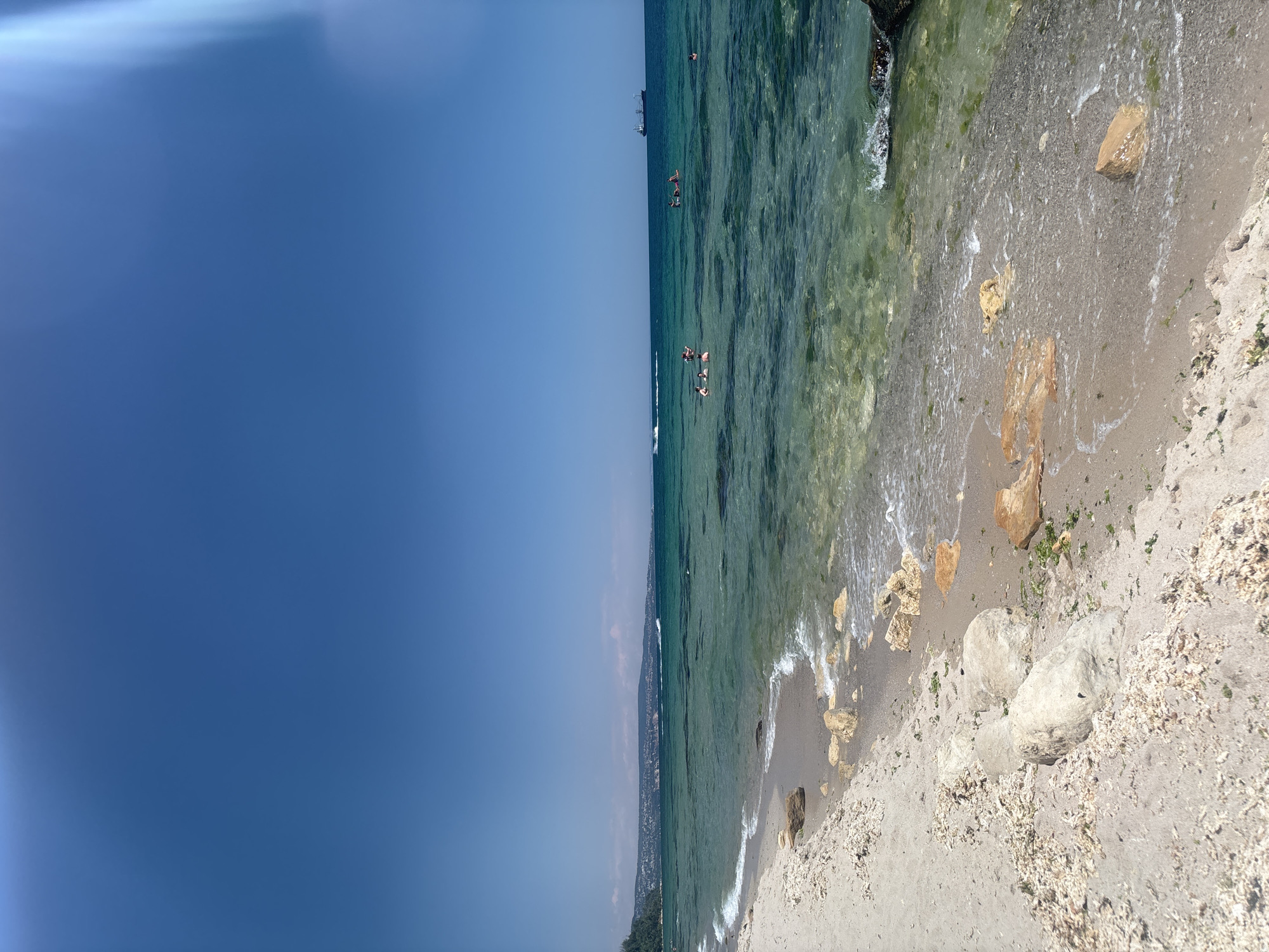 Calm turquoise shoreline with rocky sand under clear skies