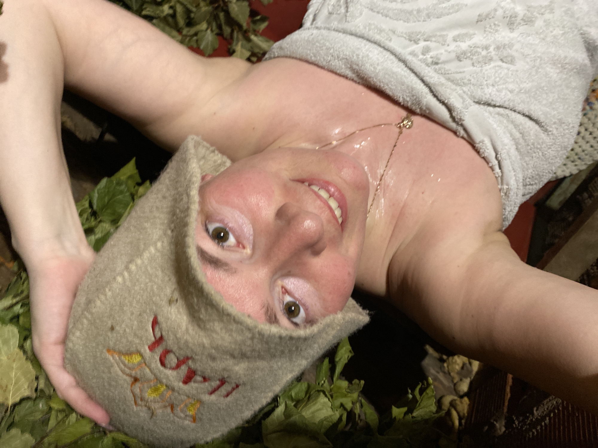 Person in sauna hat rests among leaves in Russia