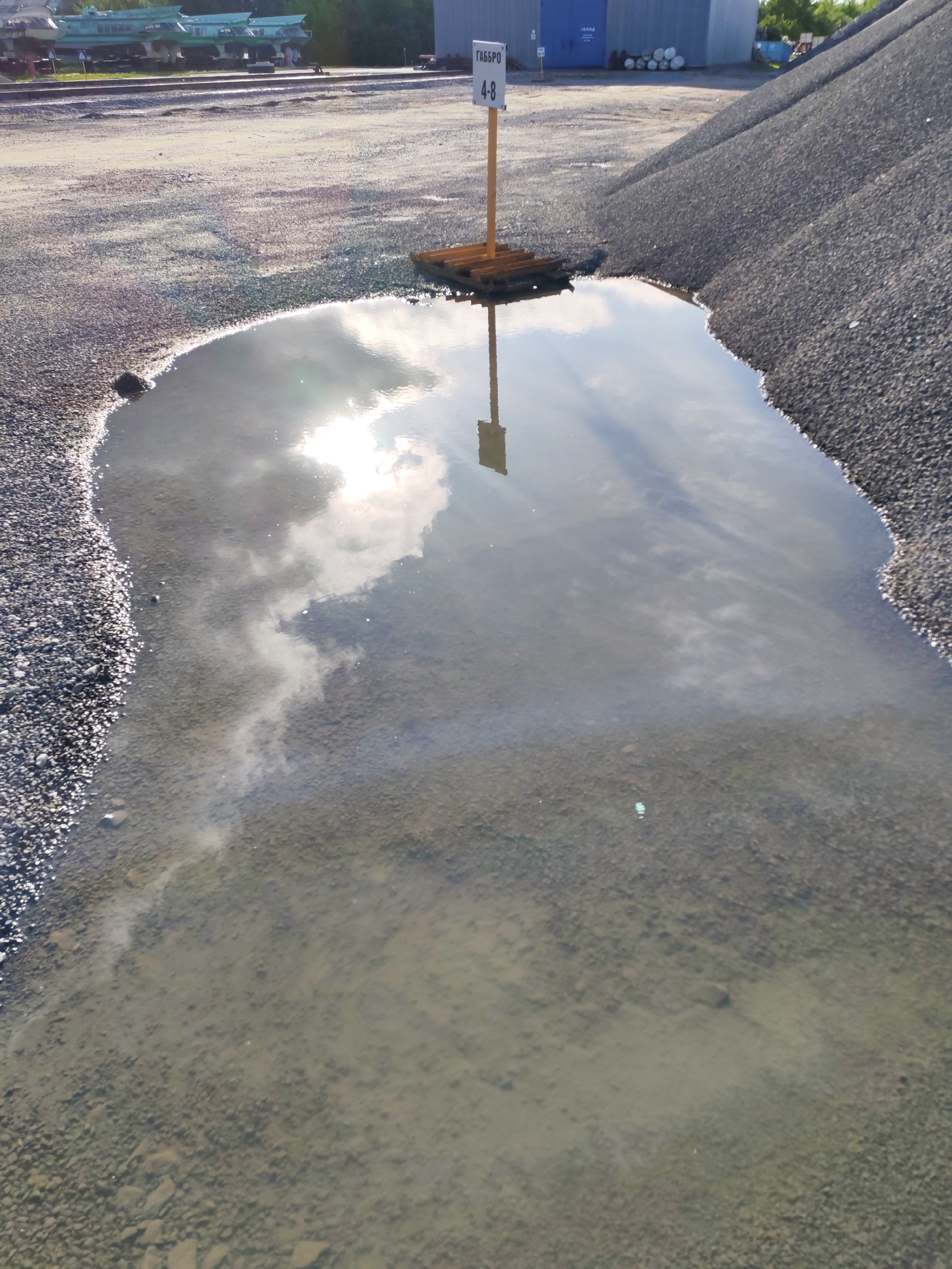 Post-rain puddles reflect sky at industrial site