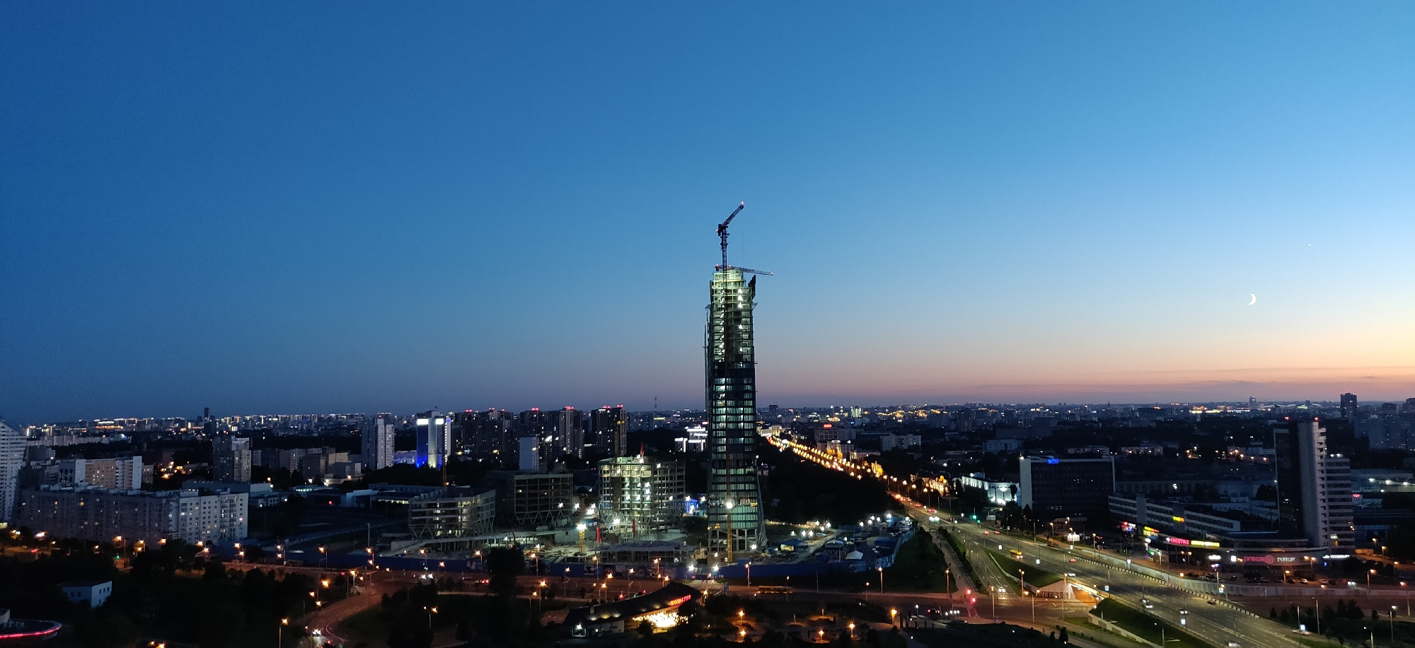 Minsk skyline at dusk: construction crane and neon-lit DANA Center