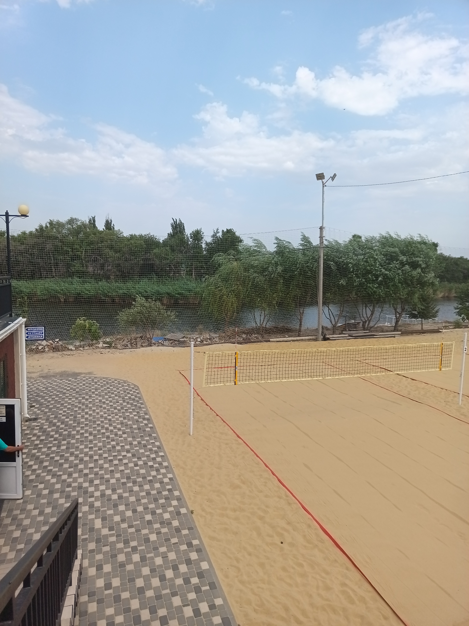 Beach volleyball court and pool area on a partly cloudy afternoon