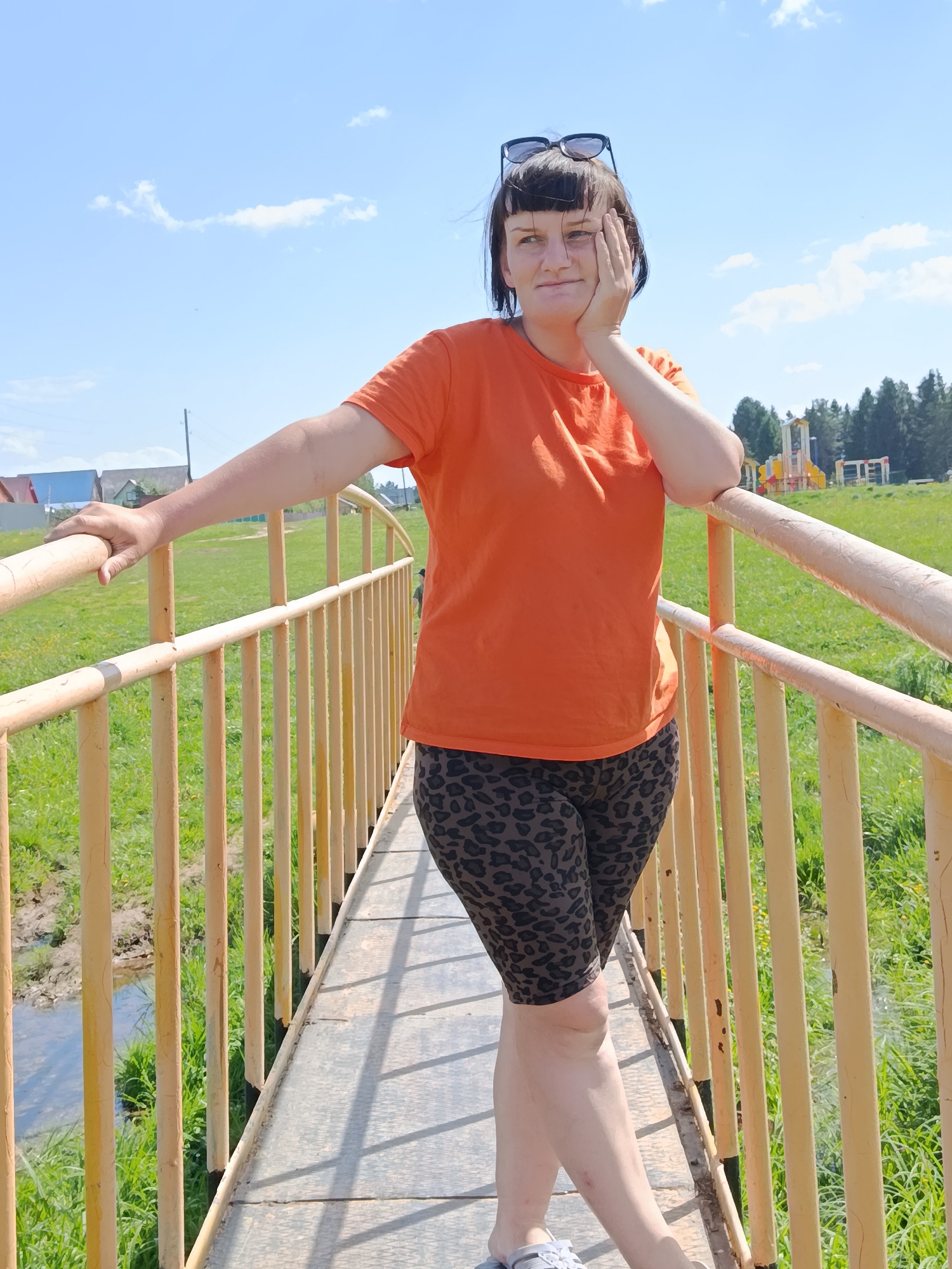 Woman in orange shirt photographed at bridge, kitchen locations