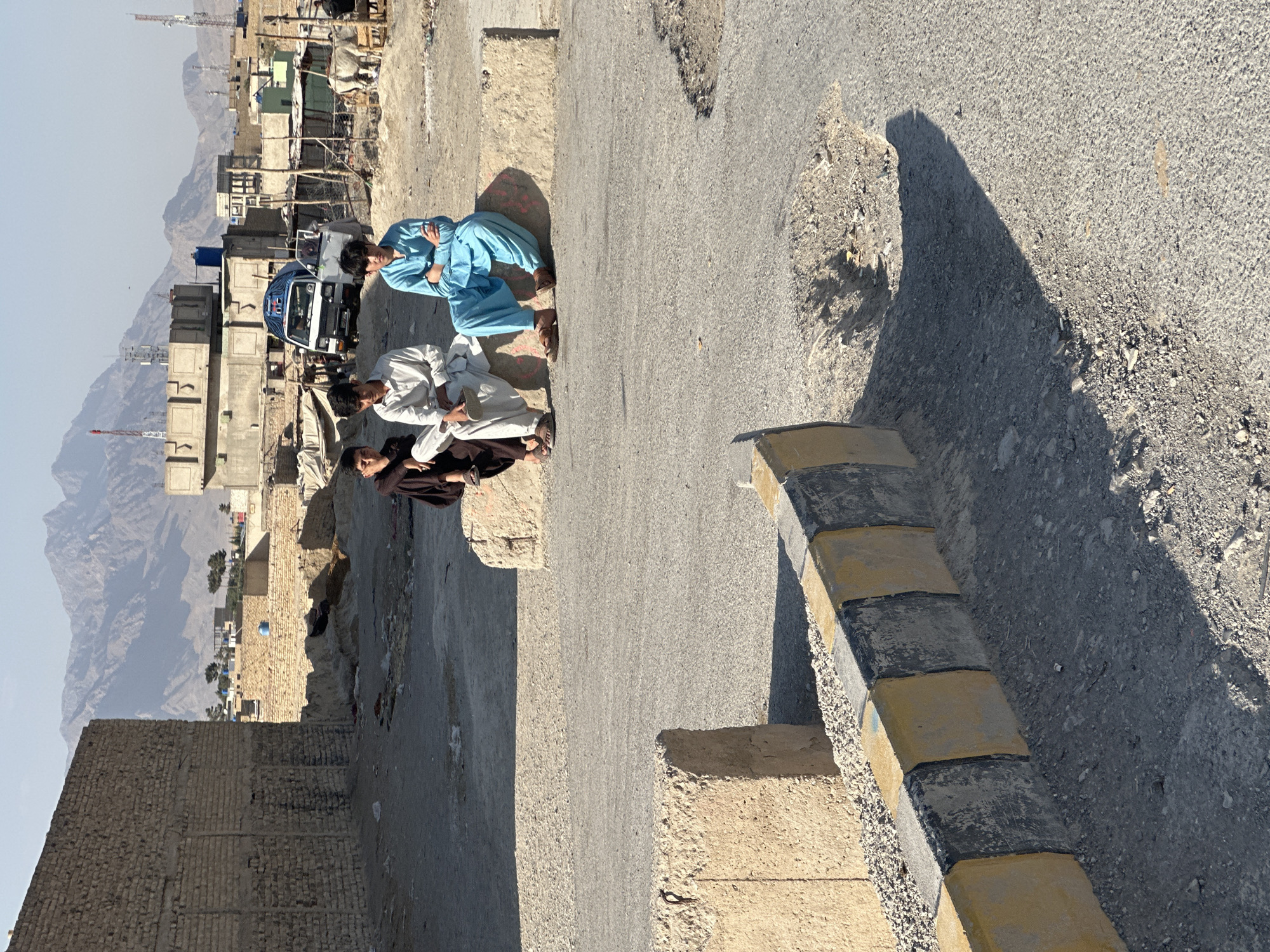 Three people on concrete barrier in dusty Quetta streets