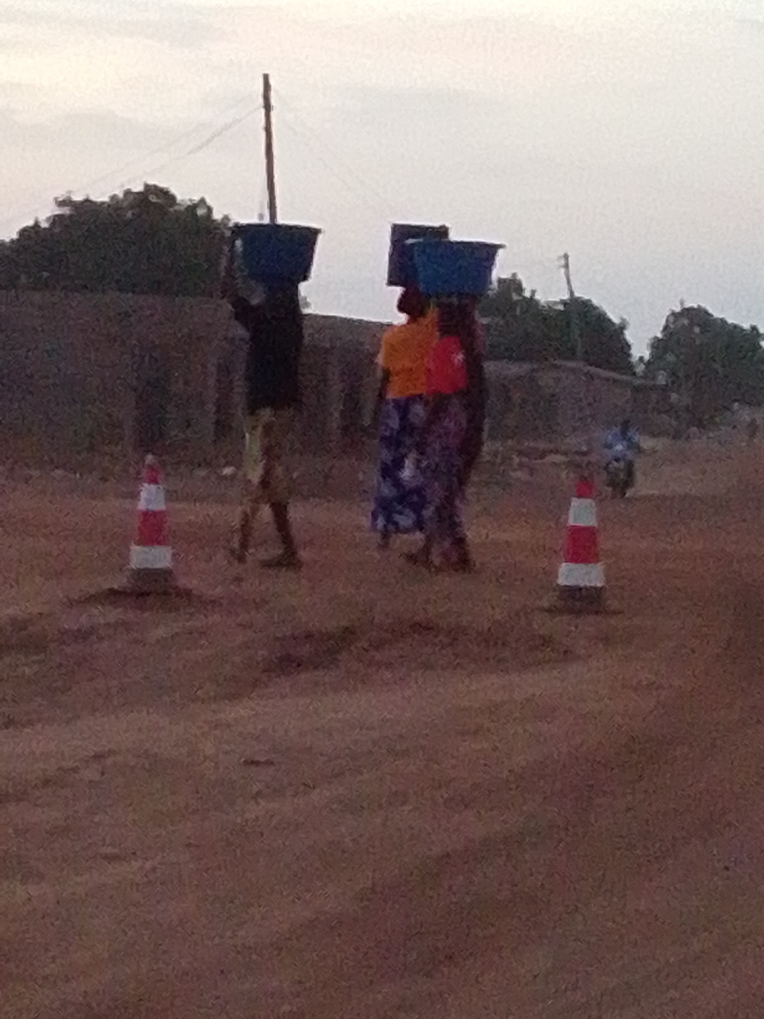 Three people carry blue containers on dirt road