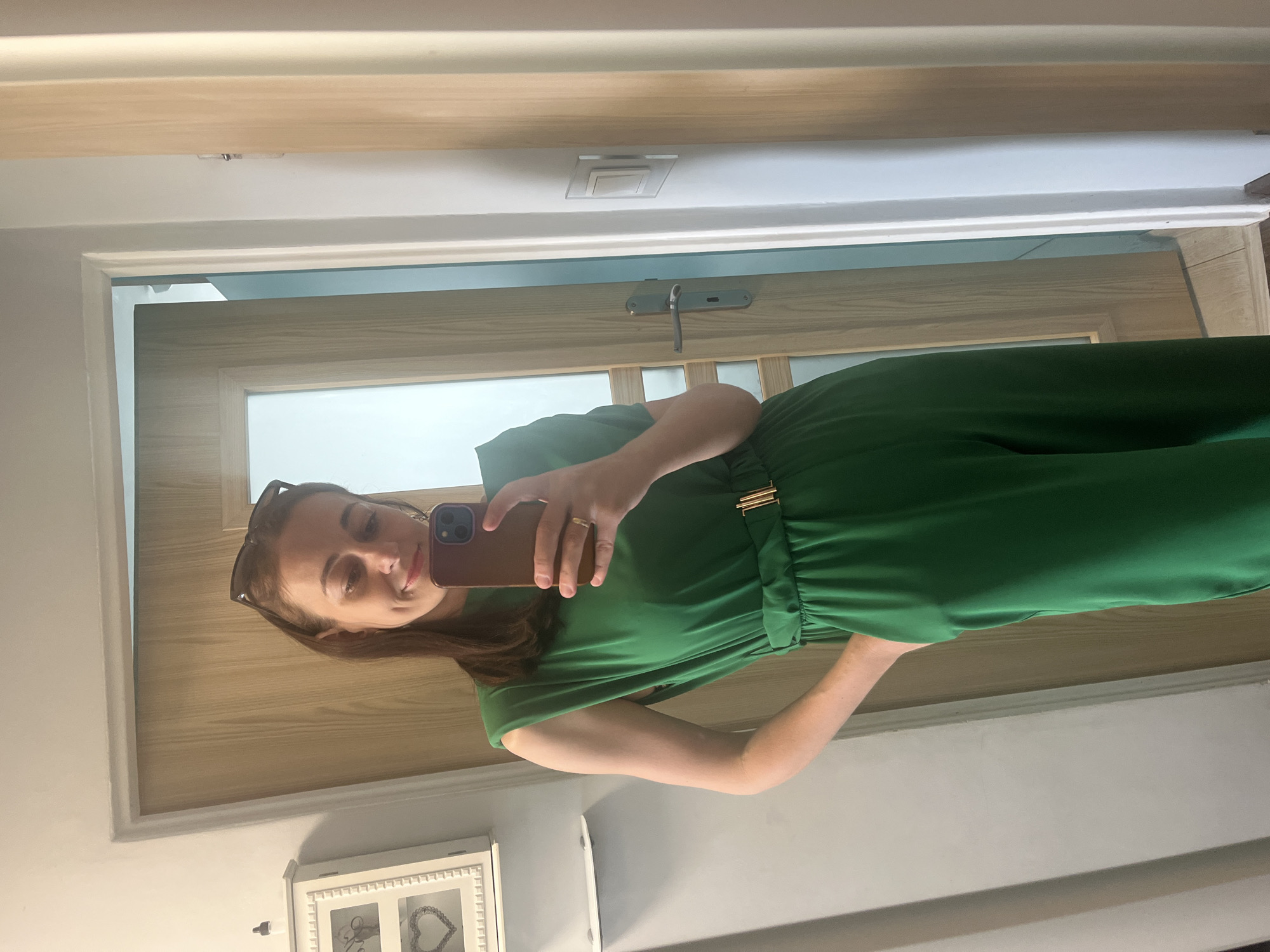 Woman documents green jumpsuit outfit in extended hallway mirror selfie session