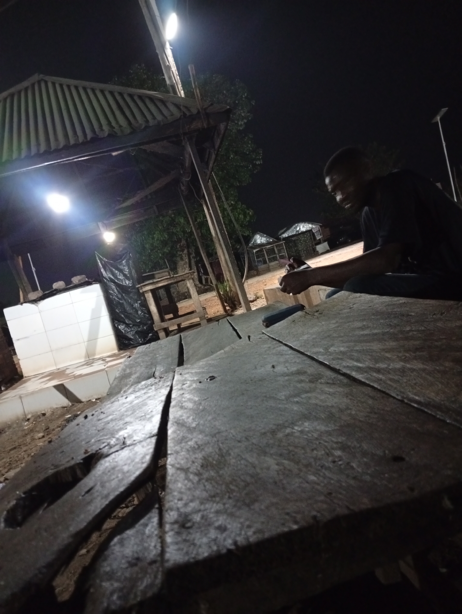 Man sits on wooden table at night in Adankolo