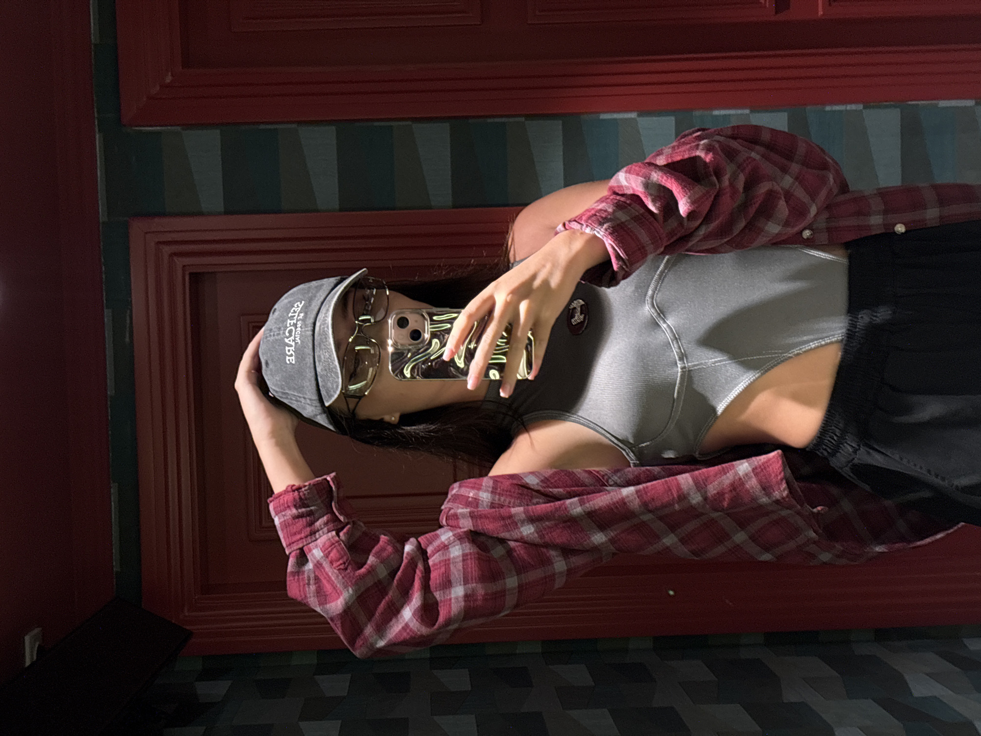 Mirror selfie in a dim room, layered plaid and cutout top