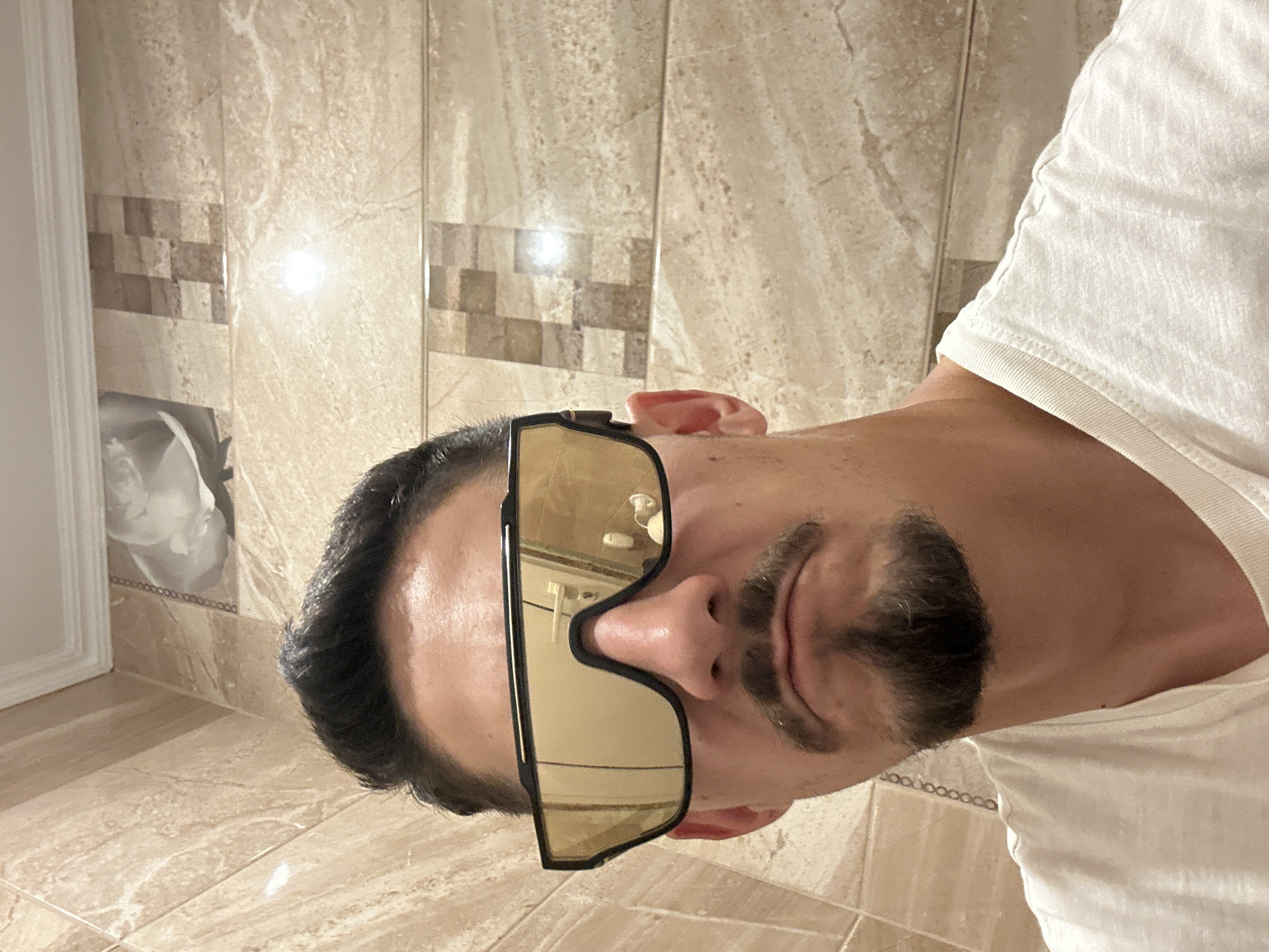 Man in sunglasses observed standing in beige-tiled bathroom