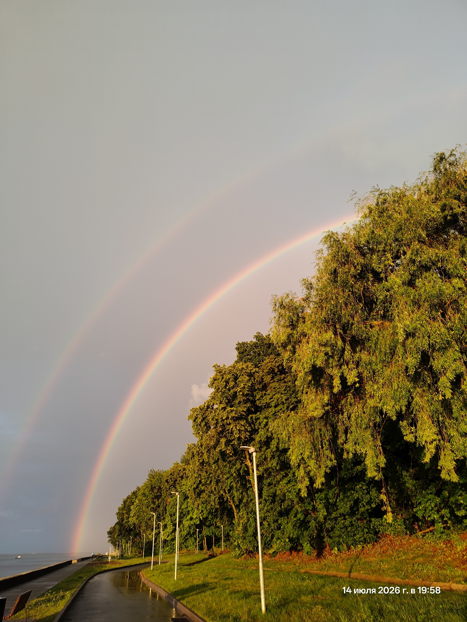 Double rainbow over a wet waterfront promenade at sunset