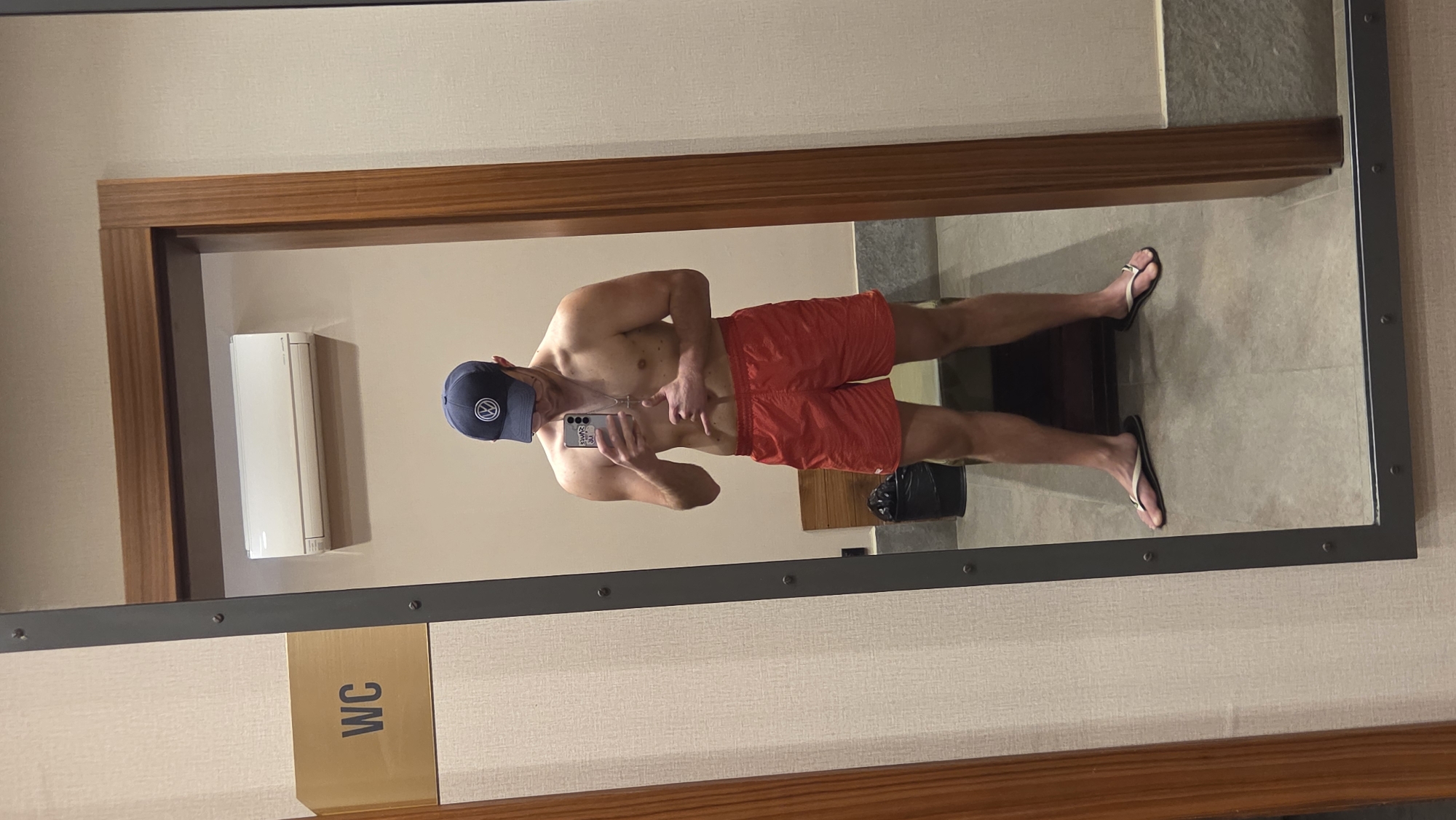 Man in lifeguard gear takes bathroom mirror selfies