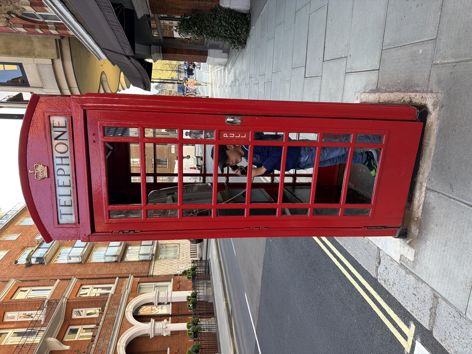 Child poses in red phone booth as family crosses London street