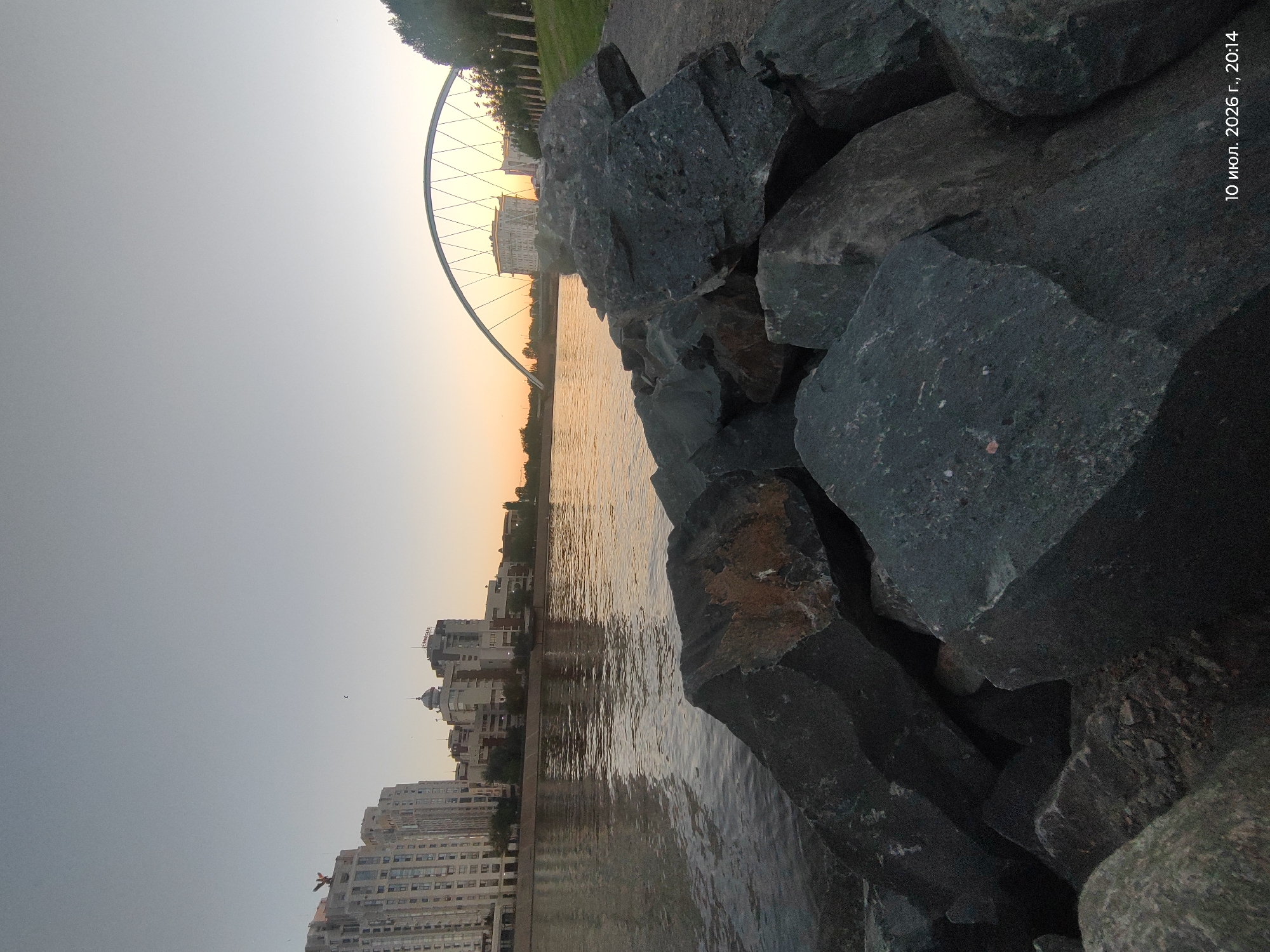 Astana riverfront at golden hour: water, skyline, and statue