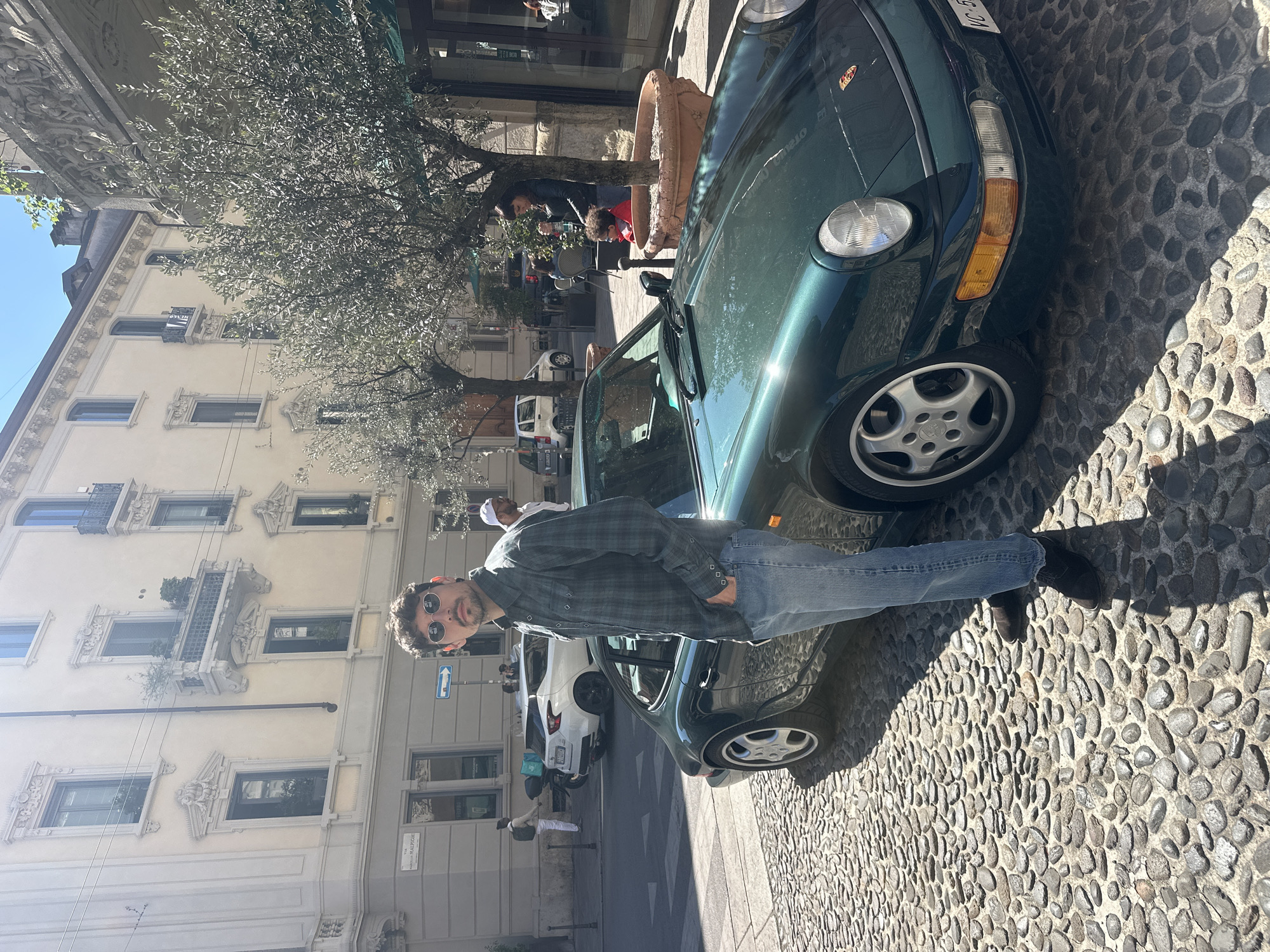 Man poses with green Porsche on Milan cobblestone street