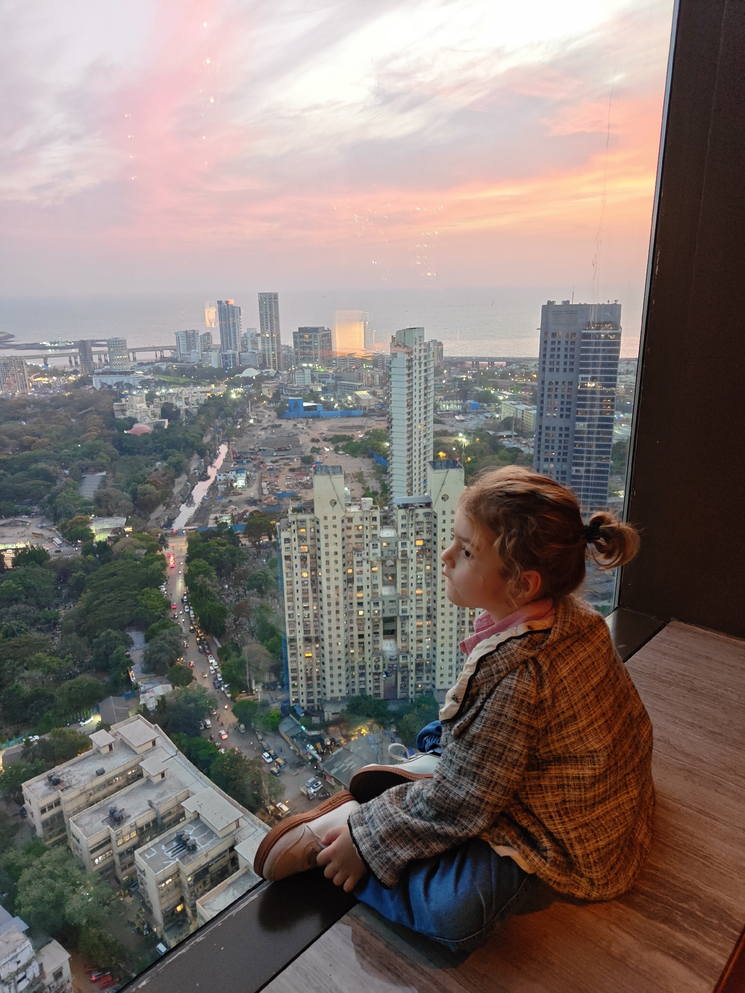 Child watches Mumbai sunset from window ledge during cityscape viewing