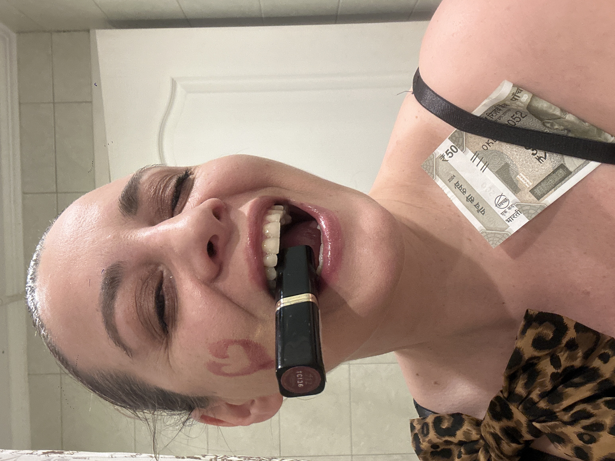 Woman applies makeup in Riga bathroom, Indian currency visible