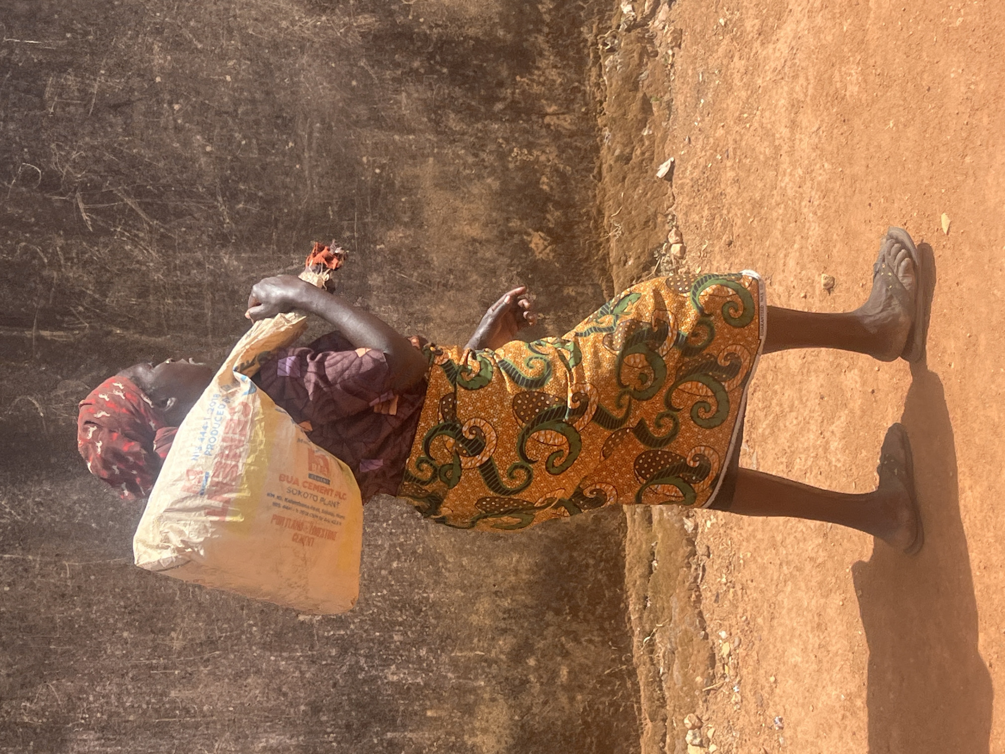 Woman carries heavy sack on dirt path in Nigeria