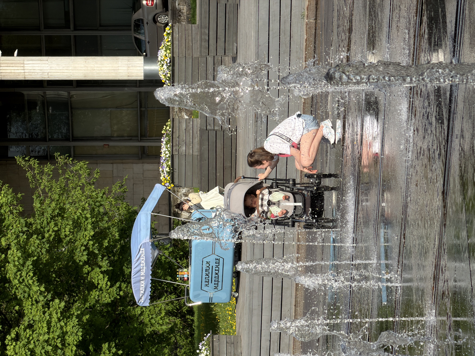 Woman with stroller pauses at Moscow fountain near beverage stand
