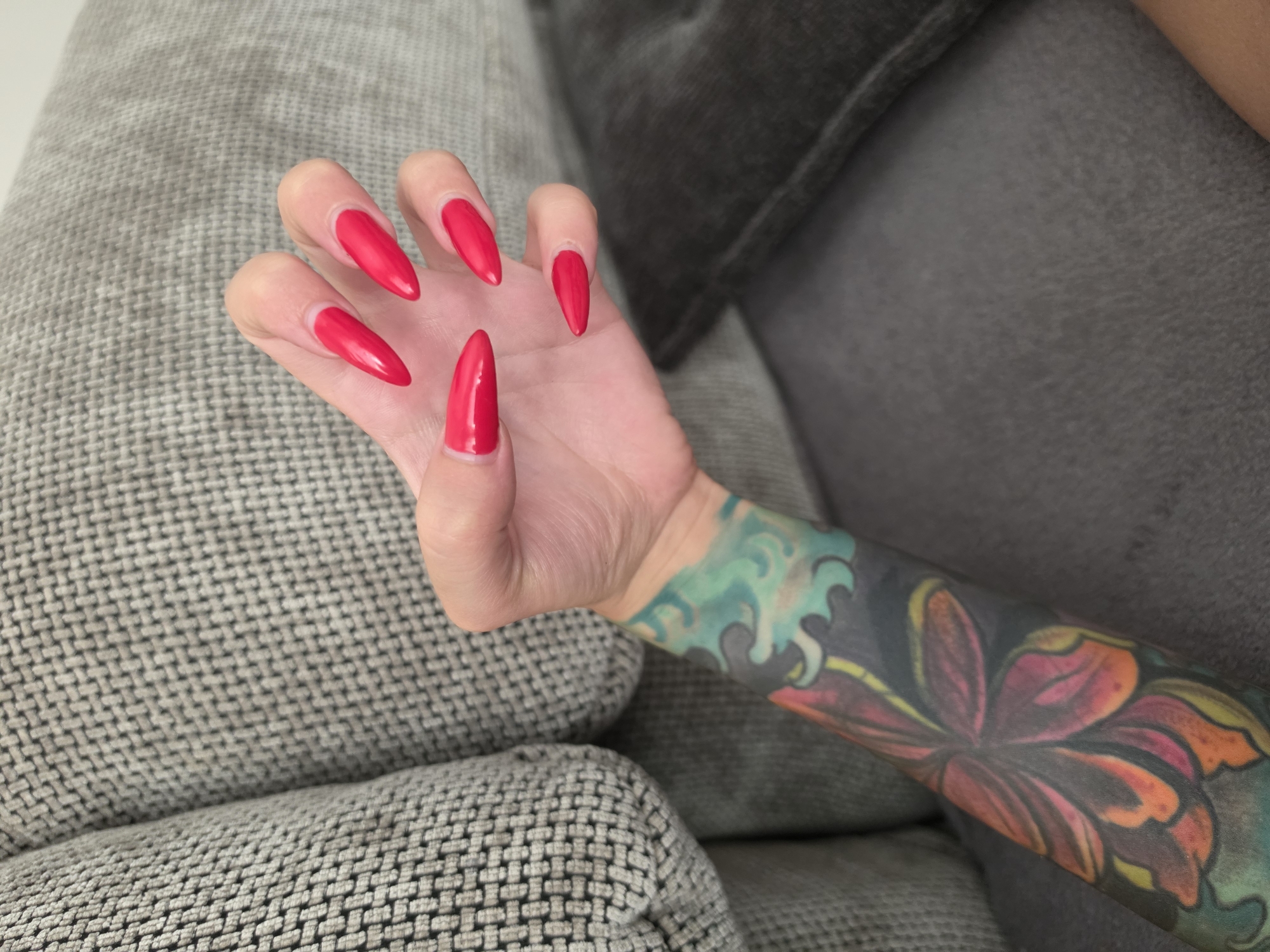 Red nails, Elsa dolls, and a tattoo on a grey couch