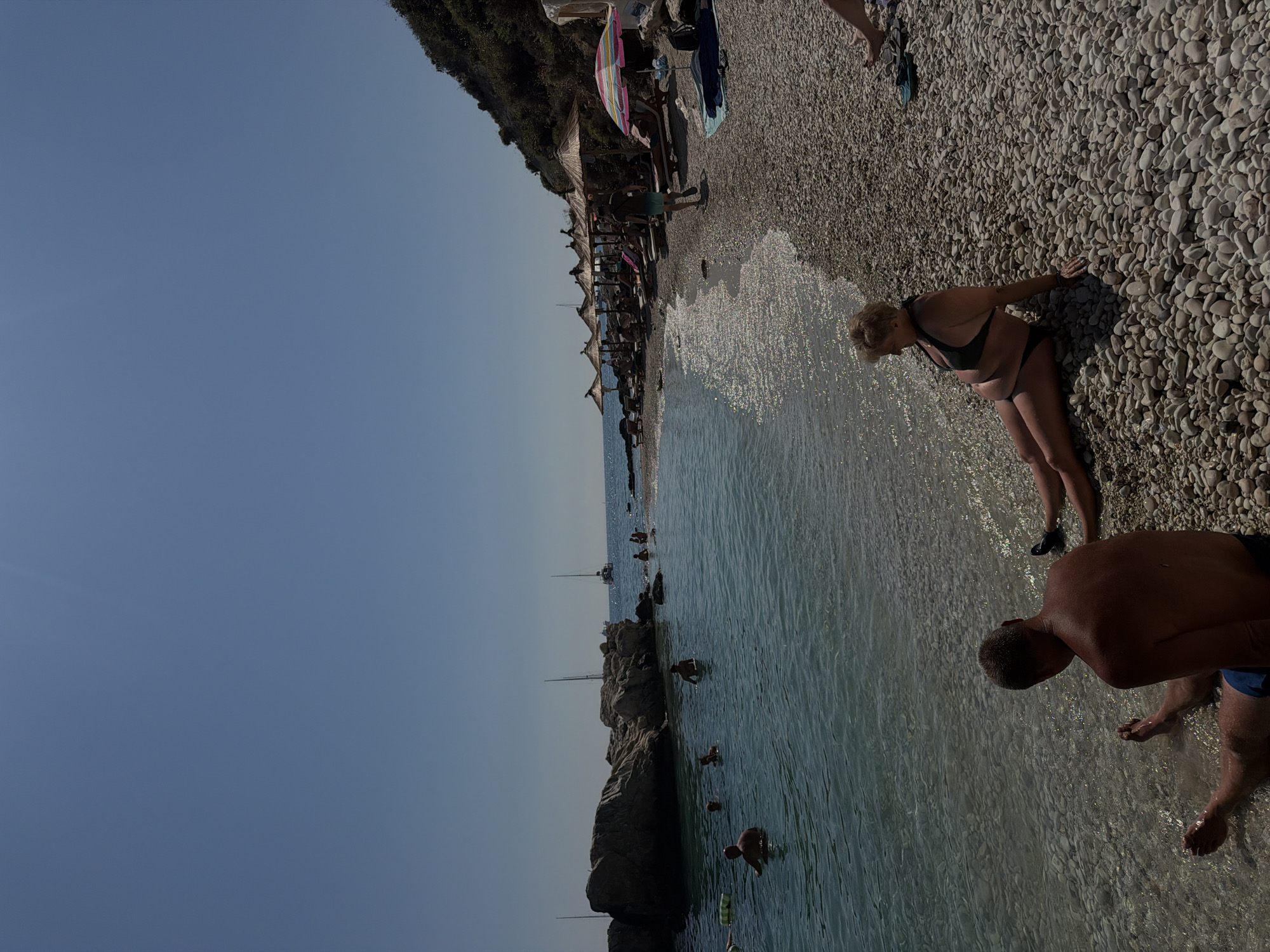 Busy Mediterranean pebble beach on a bright summer morning